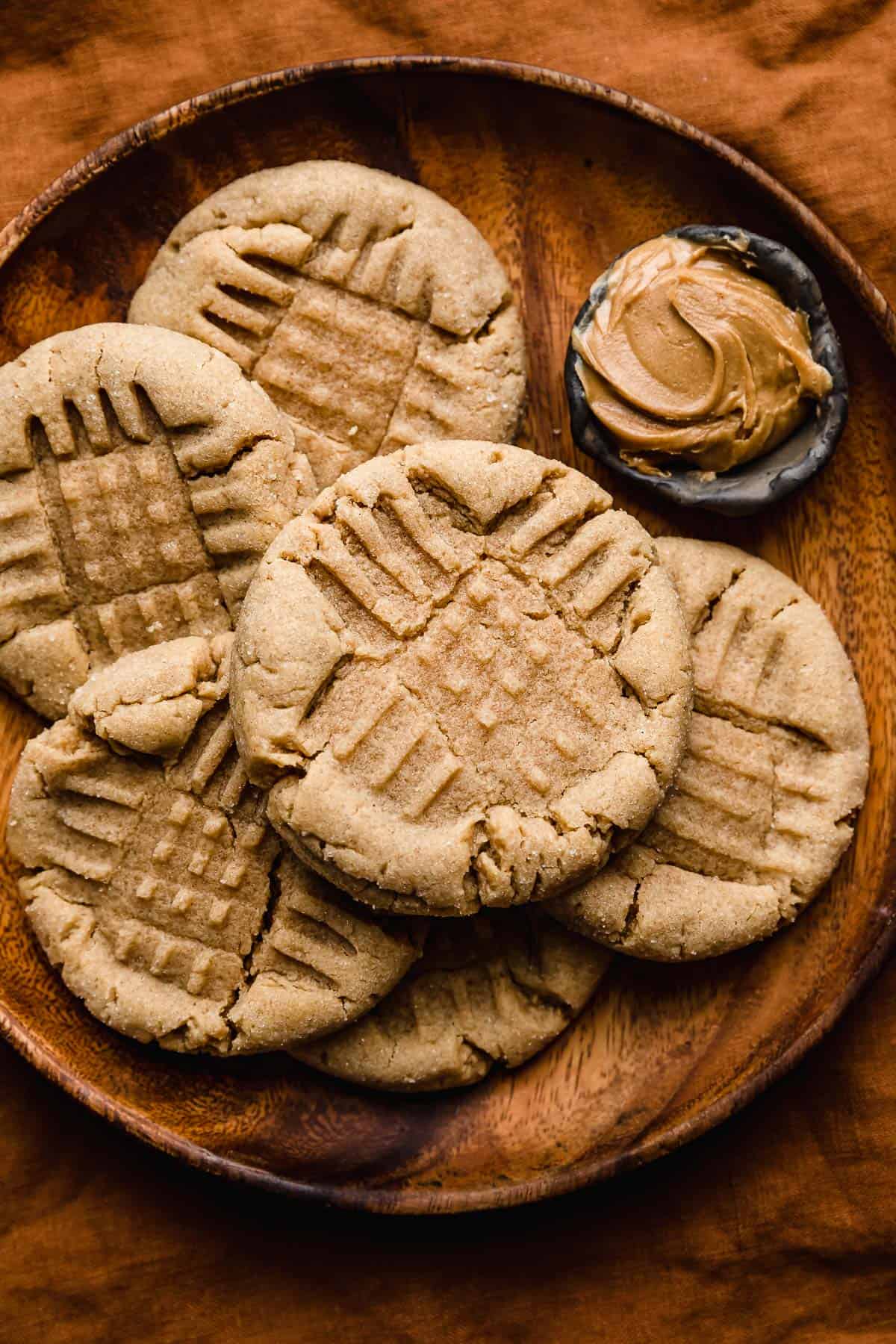 Several criss cross imprinted Peanut Butter Cookies on a round wooden plate on an amber colored background. 