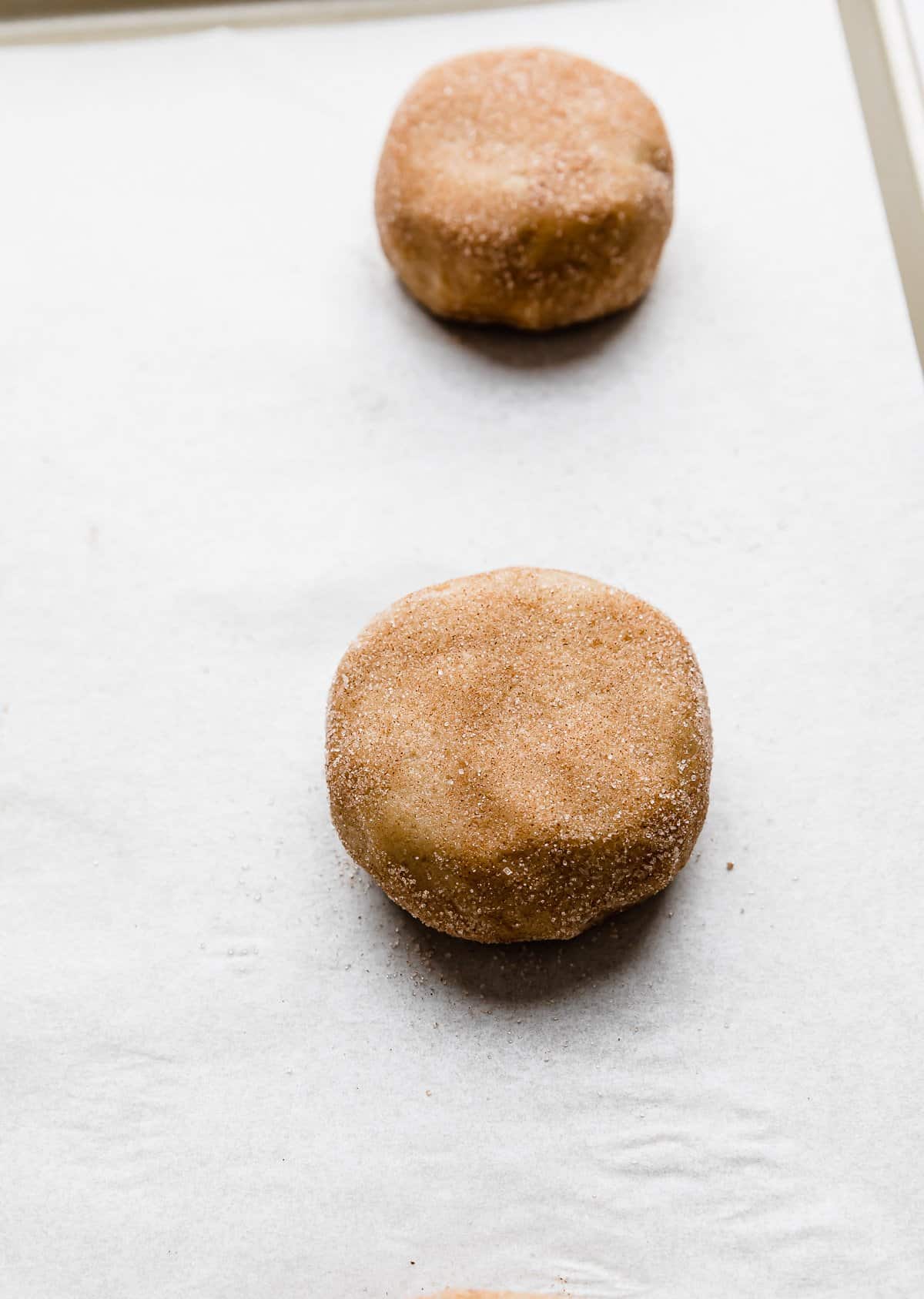 An unbaked ball of Crumbl Hazelnut Churro Cookie dough on a white parchment lined baking sheet.