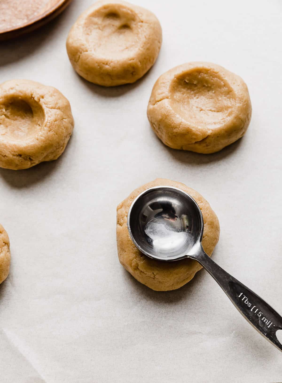 A metal tablespoon sized measuring spoon being pressed into a ball of churro cookie dough to make a copycat Crumbl Hazelnut Churro Cookies.