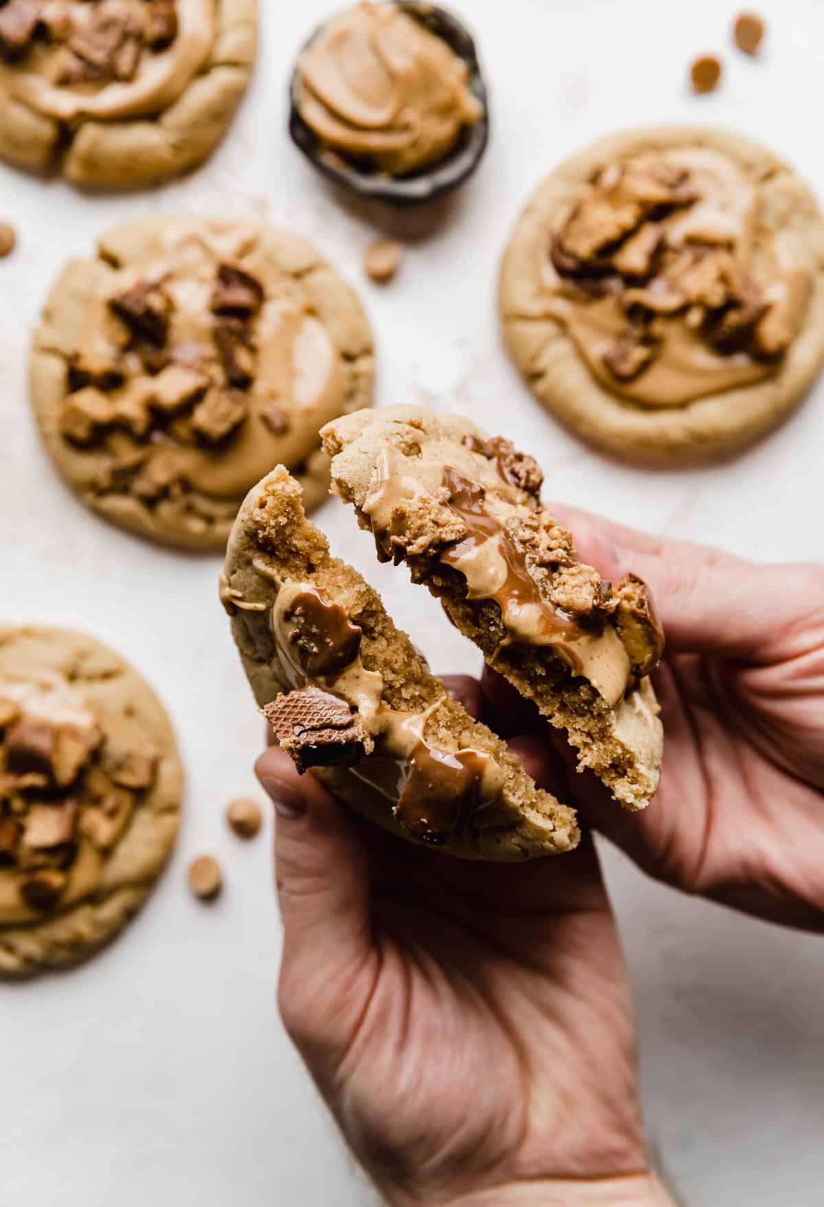 A pair of hands breaking a copycat Crumbl Peanut Butter Cup Cookie in half.