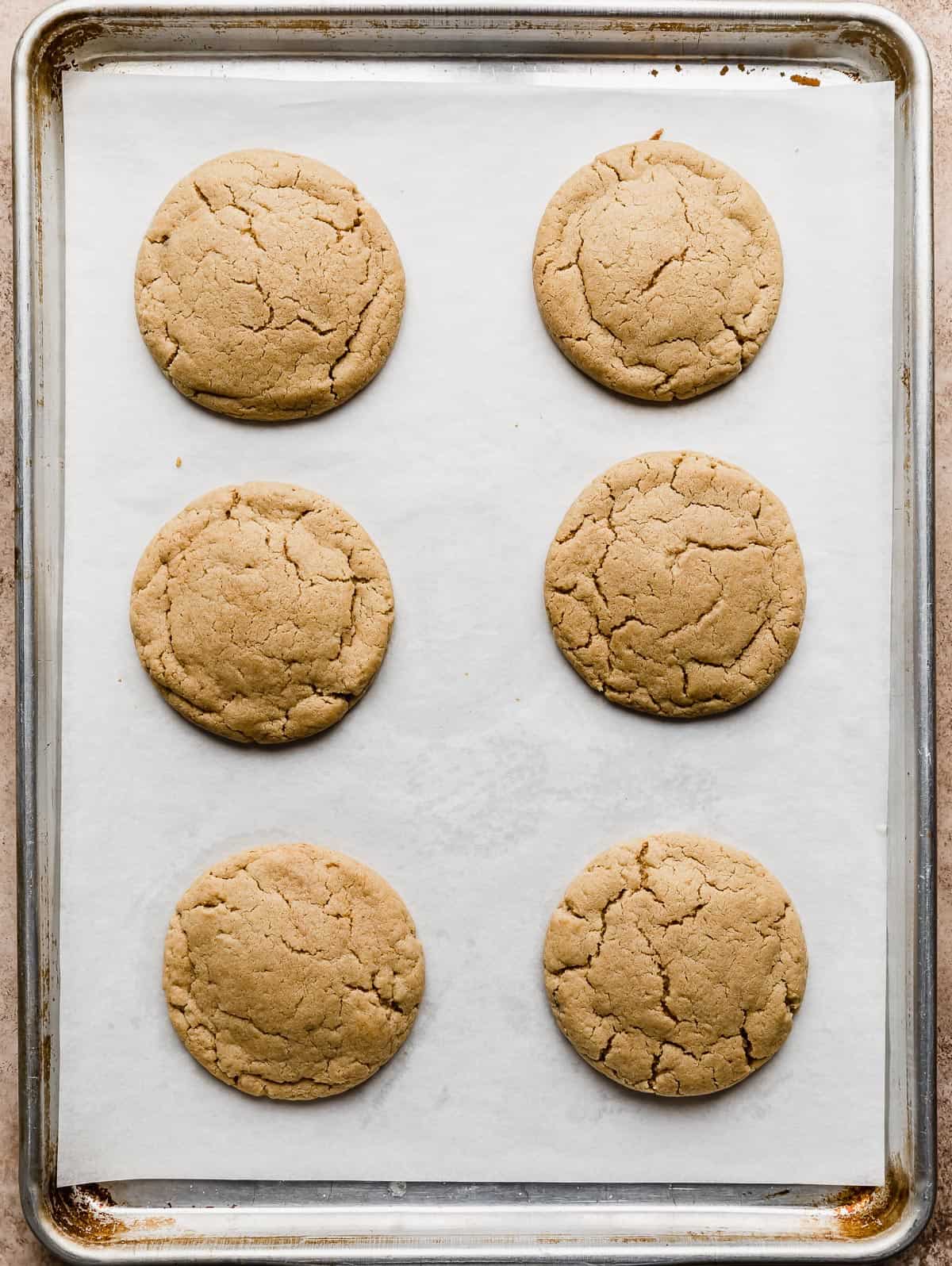 Six baked peanut butter cookies on a white parchment lined baking sheet.