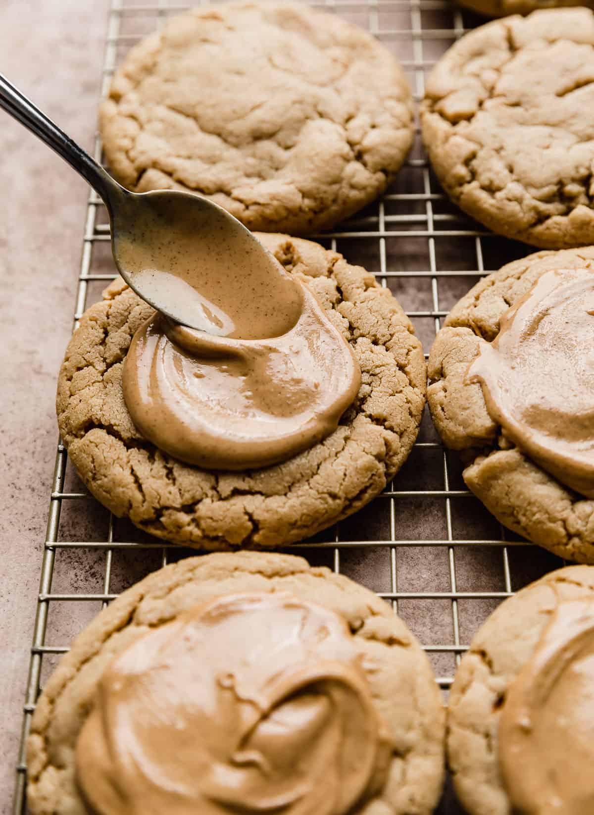 A spoon spreading melted peanut butter on top of a peanut butter cookie.