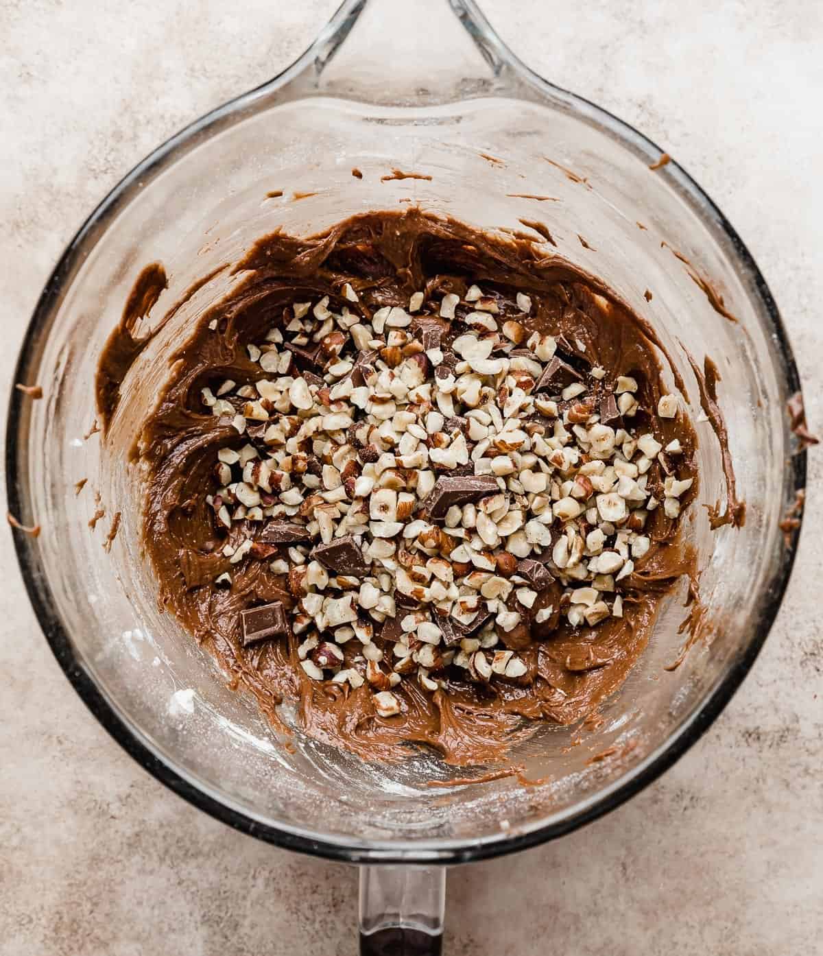 Chopped hazelnuts overtop a Nutella brownie batter in a glass bowl.