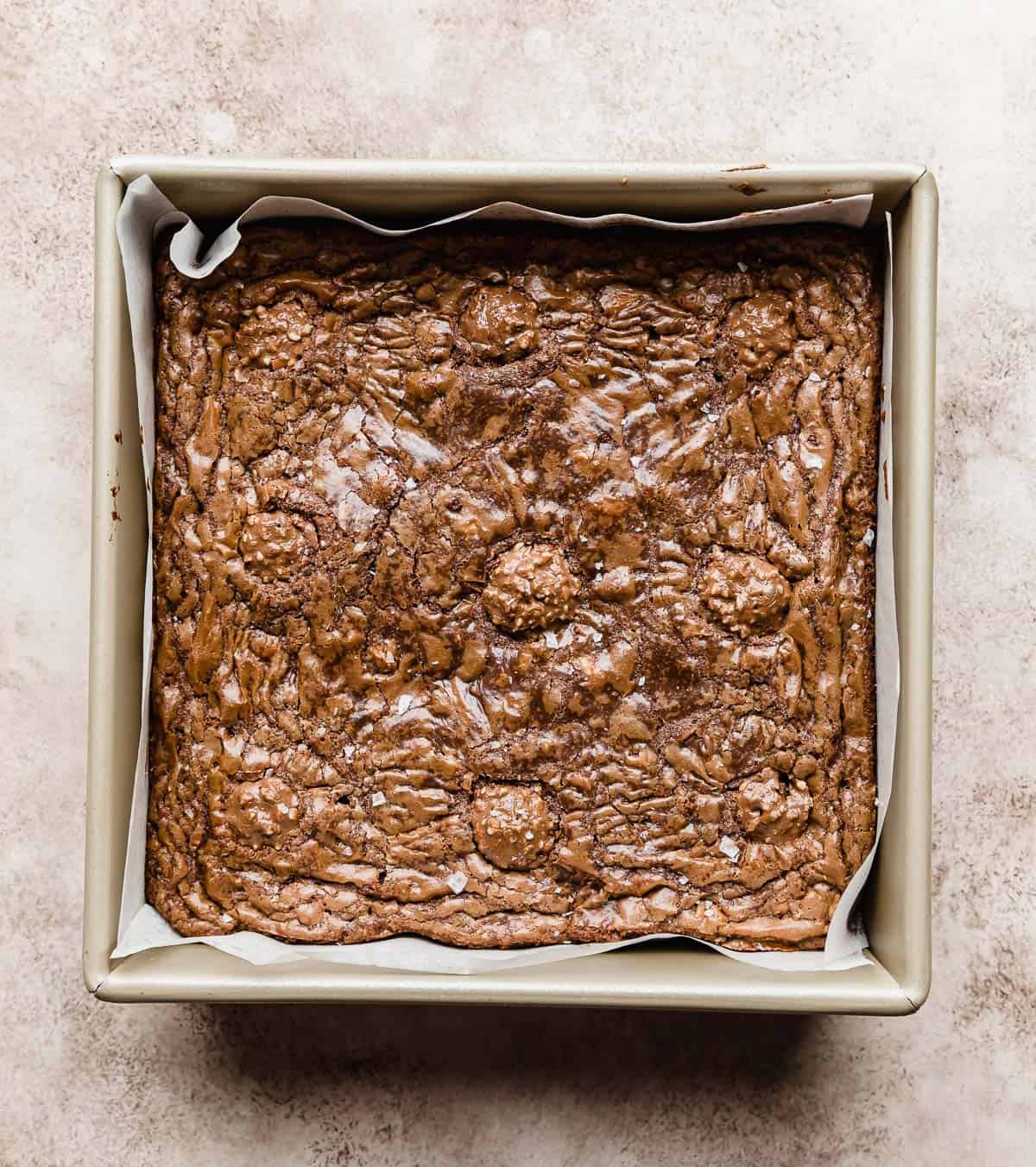 Ferrero Rocher Brownies with a crackly baked top, on a beige textured background.