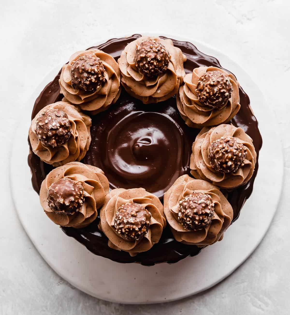 An overhead photo of a Ferrero Rocher Cake that's topped with a chocolate ganache and swirls of chocolate frosting garnished with unwrapped Ferrero Rocher candies.