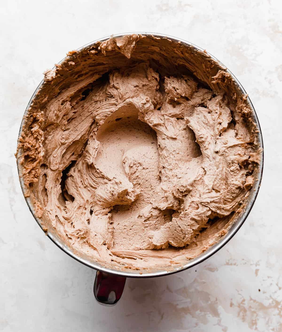 Chocolate buttercream frosting in a metal stand mixer bowl on a white background.
