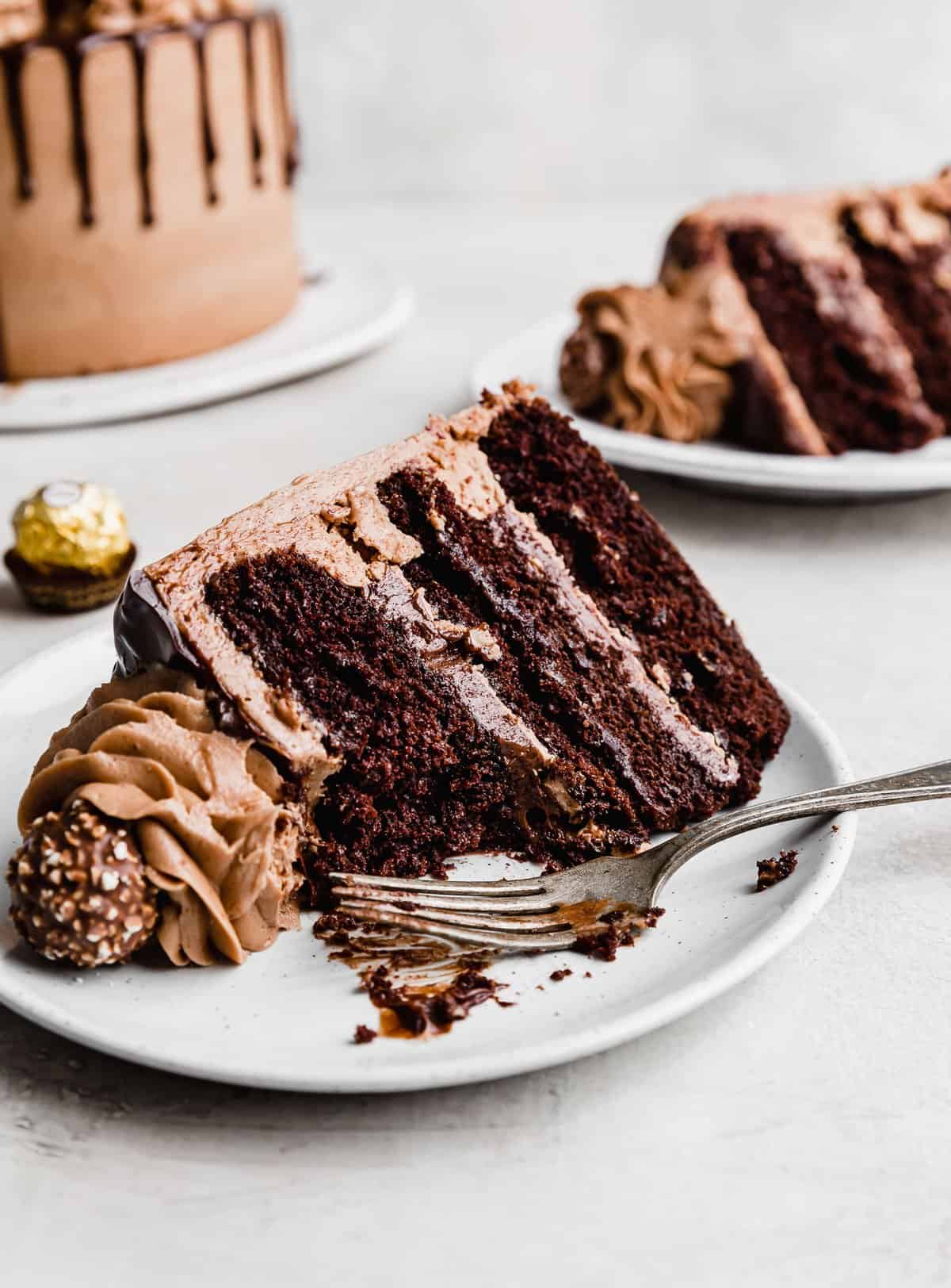 A chocolate hazelnut layer cake on a white plate with a fork next to the slice.