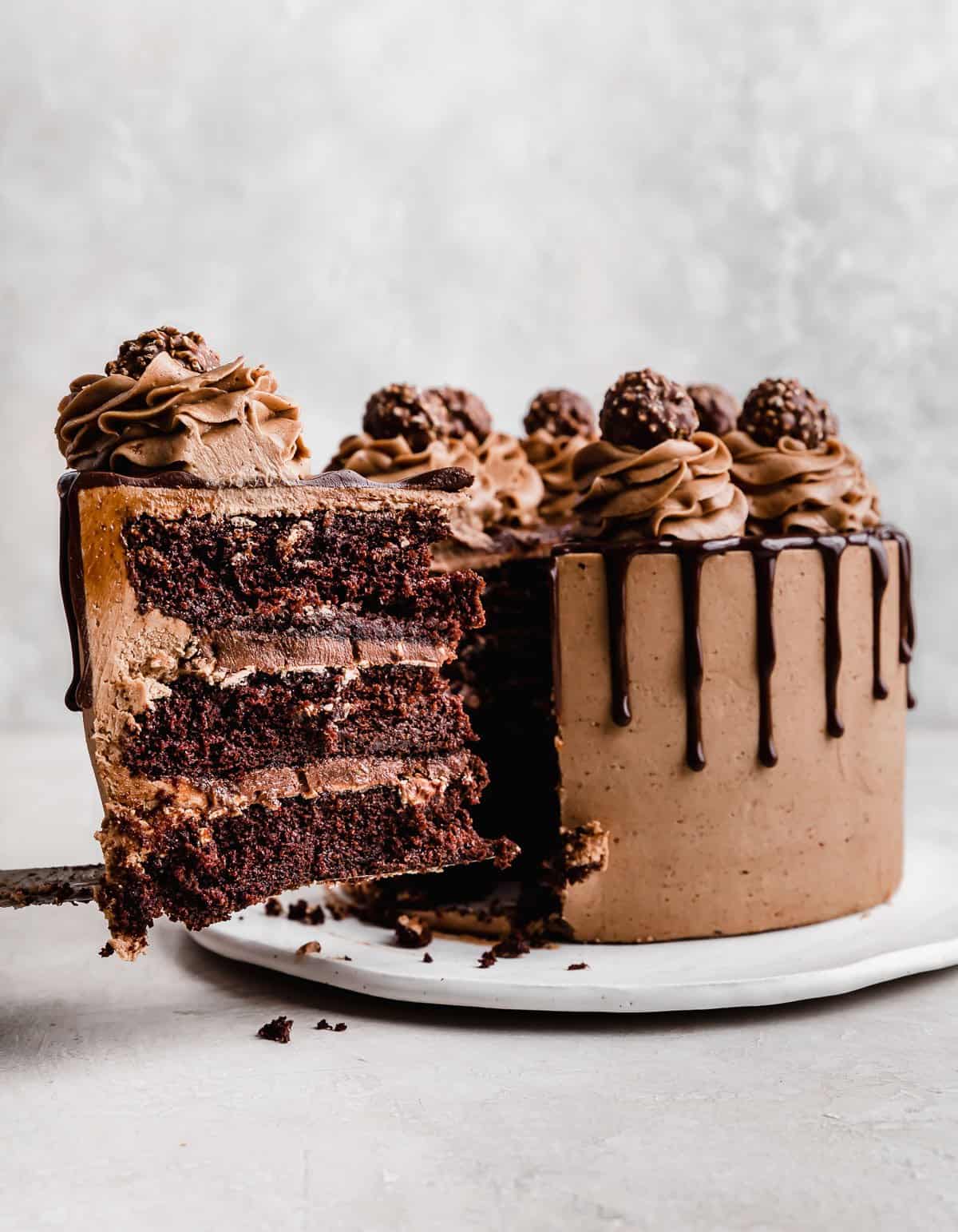 A slice of Ferrero Rocher Cake topped with chocolate buttercream and a chocolate drip.