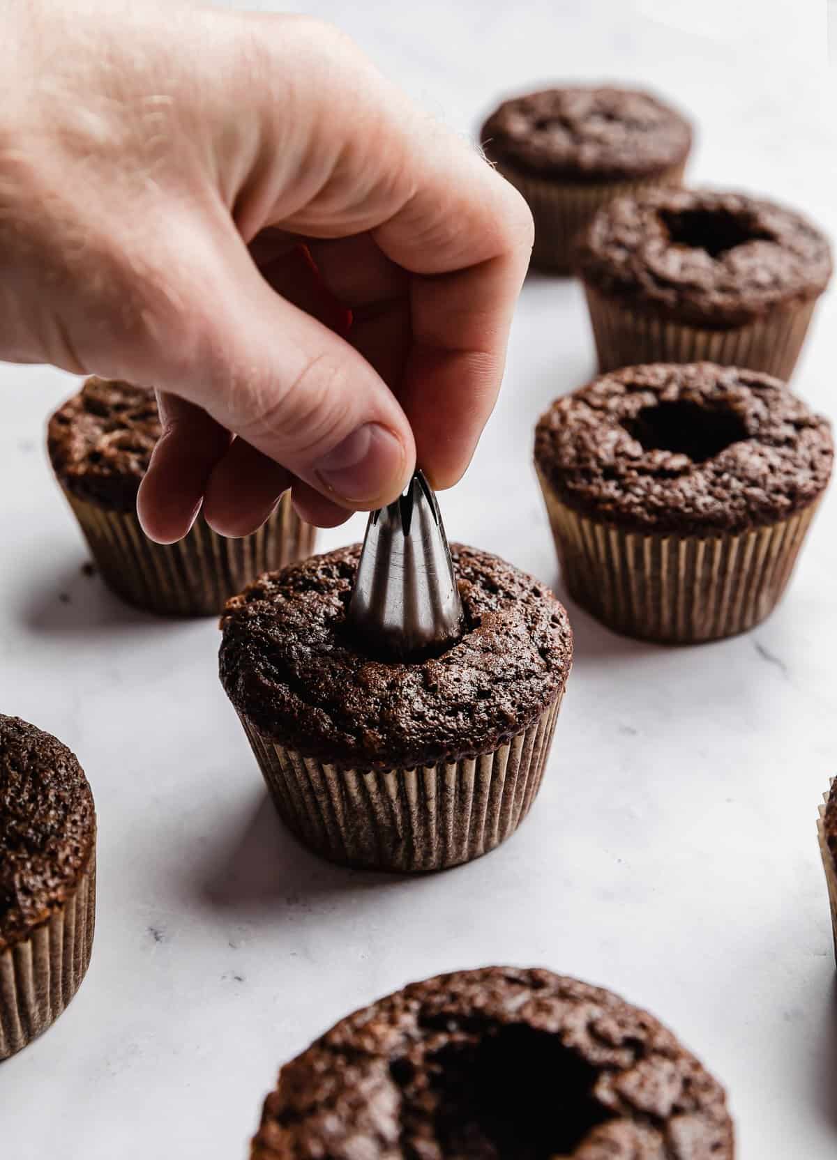 A hand using a piping tip to remove the core of a chocolate cupcake.