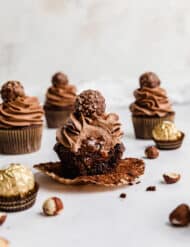 A Ferrero Rocher Cupcake with a bite taken out of it showing the inside of the cupcake filled with Nutella.