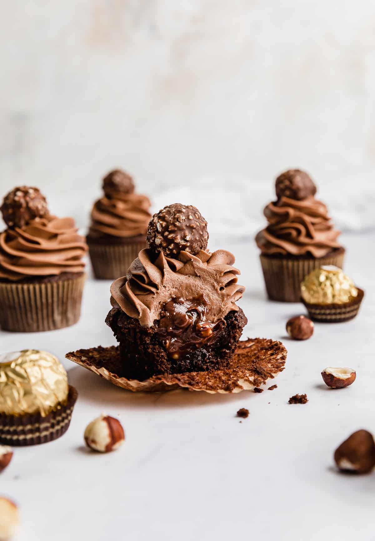 A Ferrero Rocher Cupcake with a bite taken out of it showing the inside of the cupcake filled with Nutella.