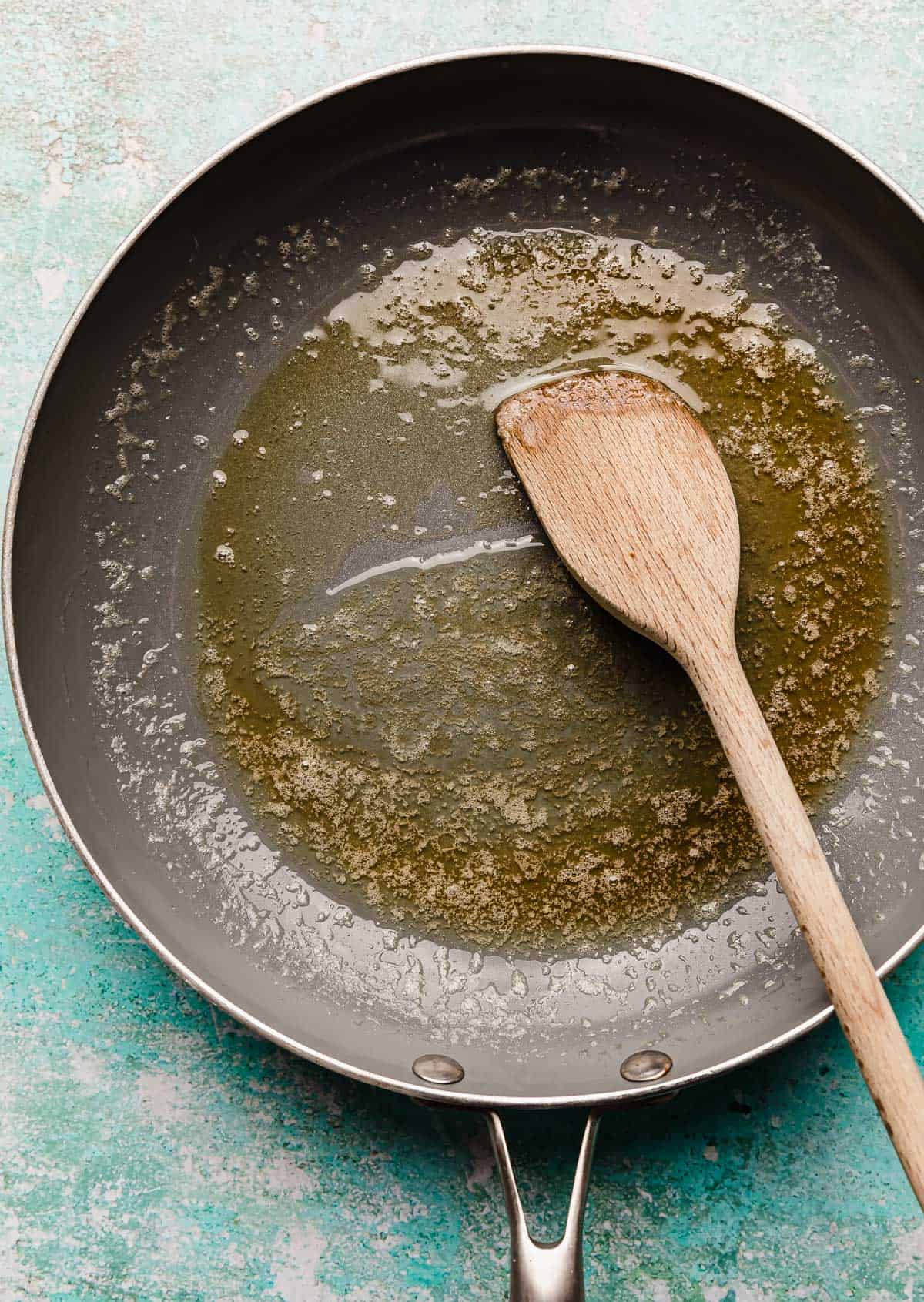 Melted butter and honey in a gray skillet on a turquoise blue background.