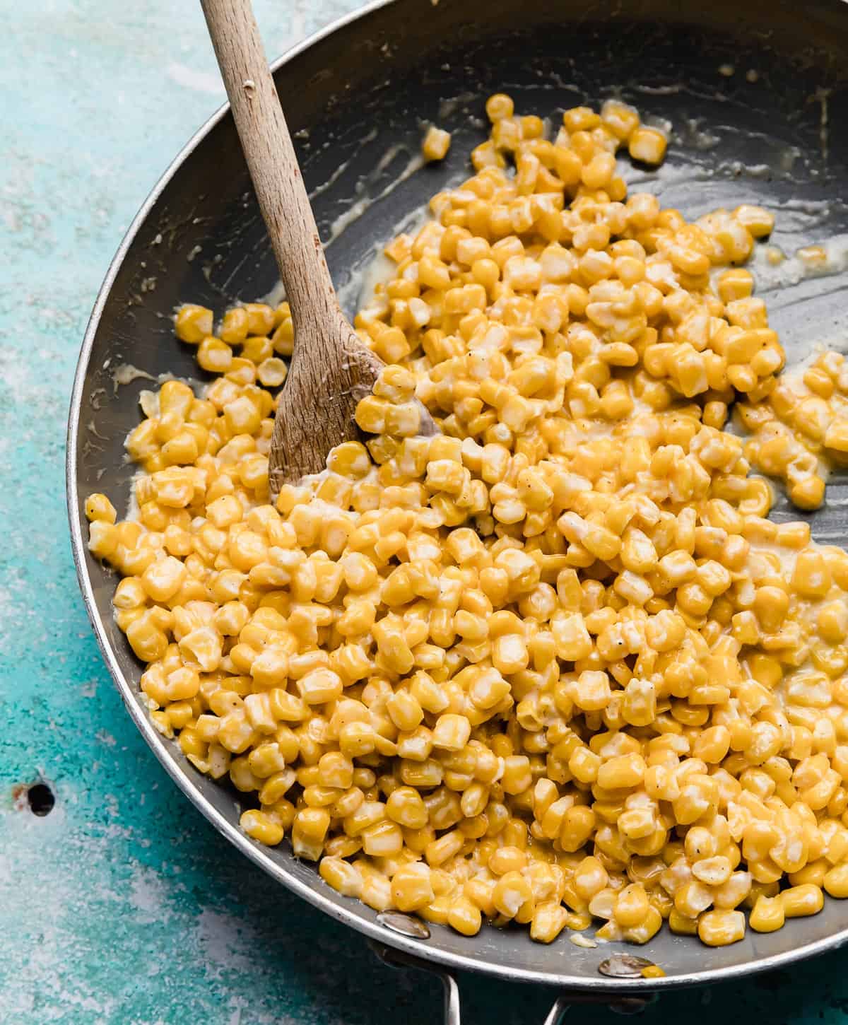 Yellow Honey Butter Skillet Corn in a gray skillet on a turquoise background.