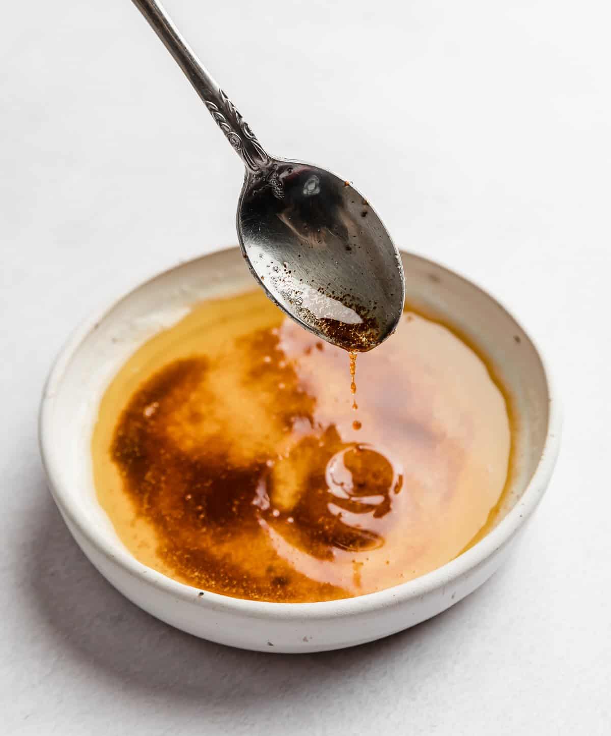 A spoon scooping up browned butter from a white bowl. 