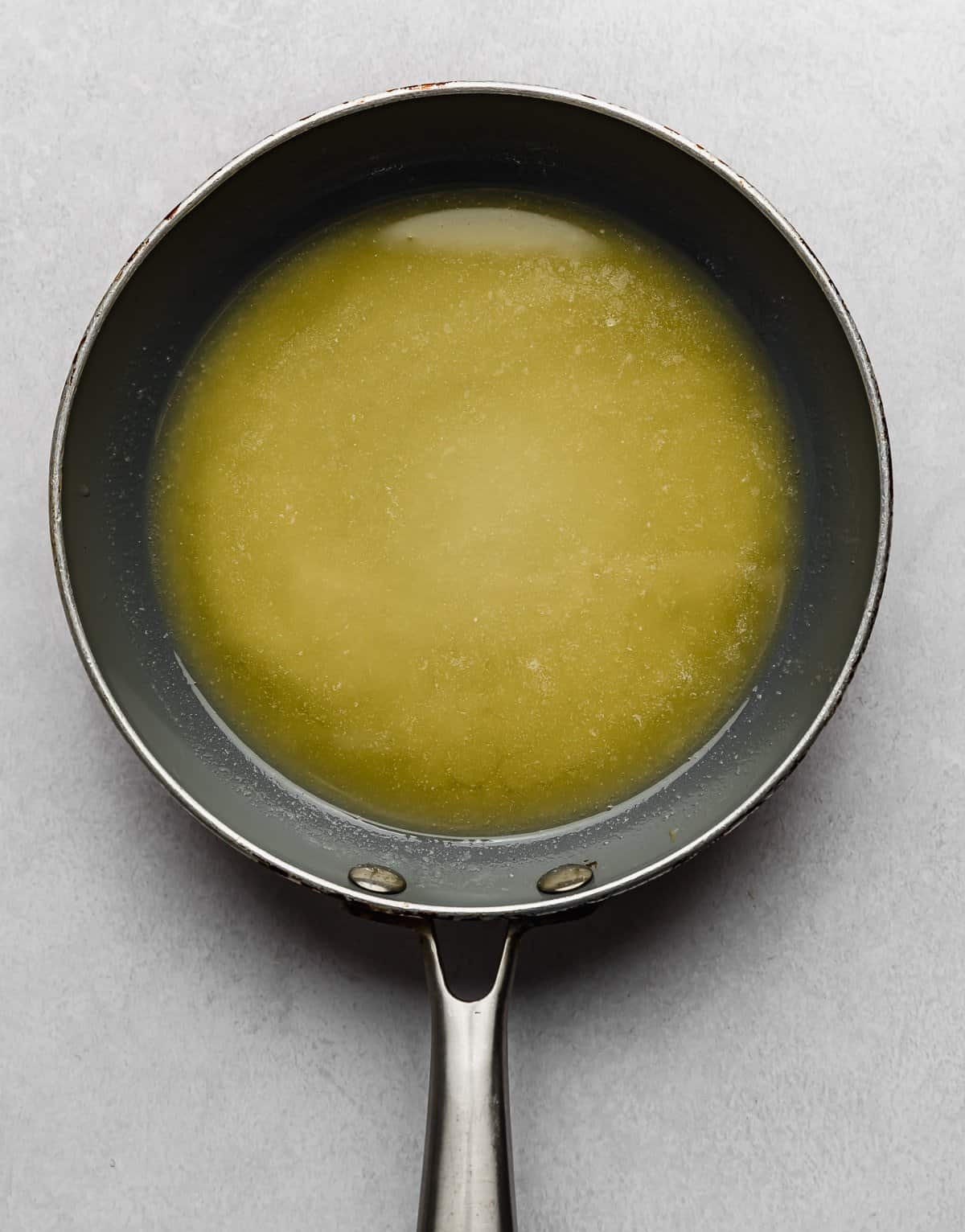 Melted butter in a grey skillet on a light grey background.