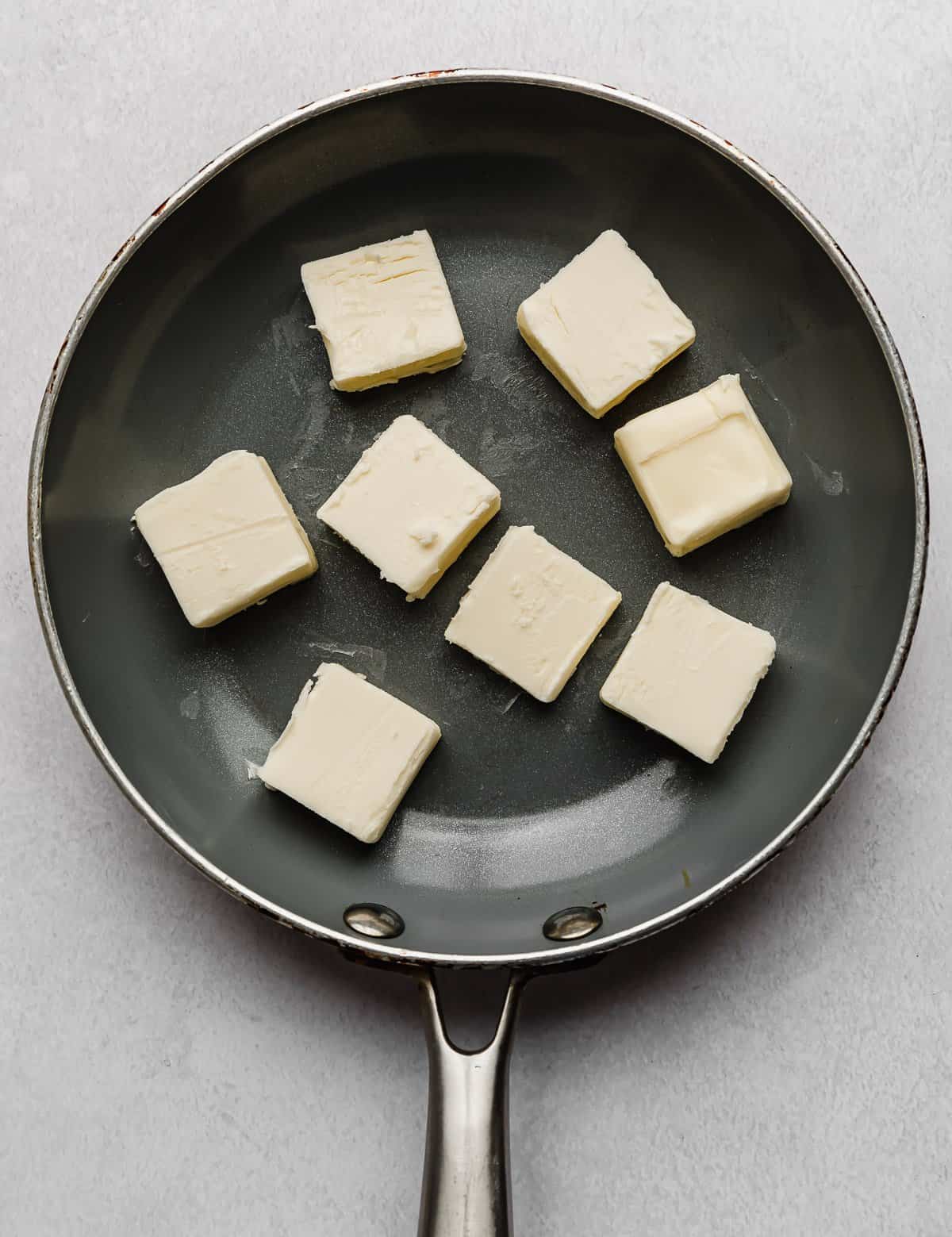 A grey skillet with eight squares of chopped butter in the skillet.