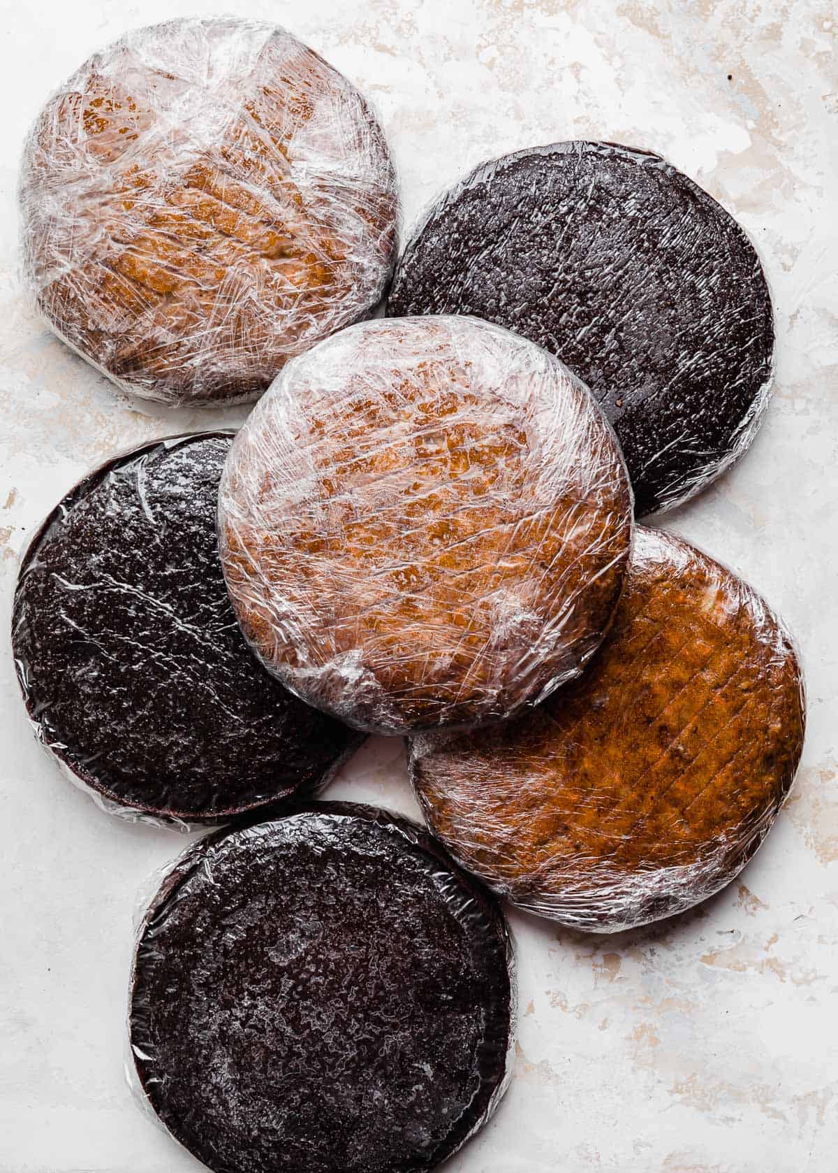 Six round cake layers individually wrapped in plastic wrap on a white background.