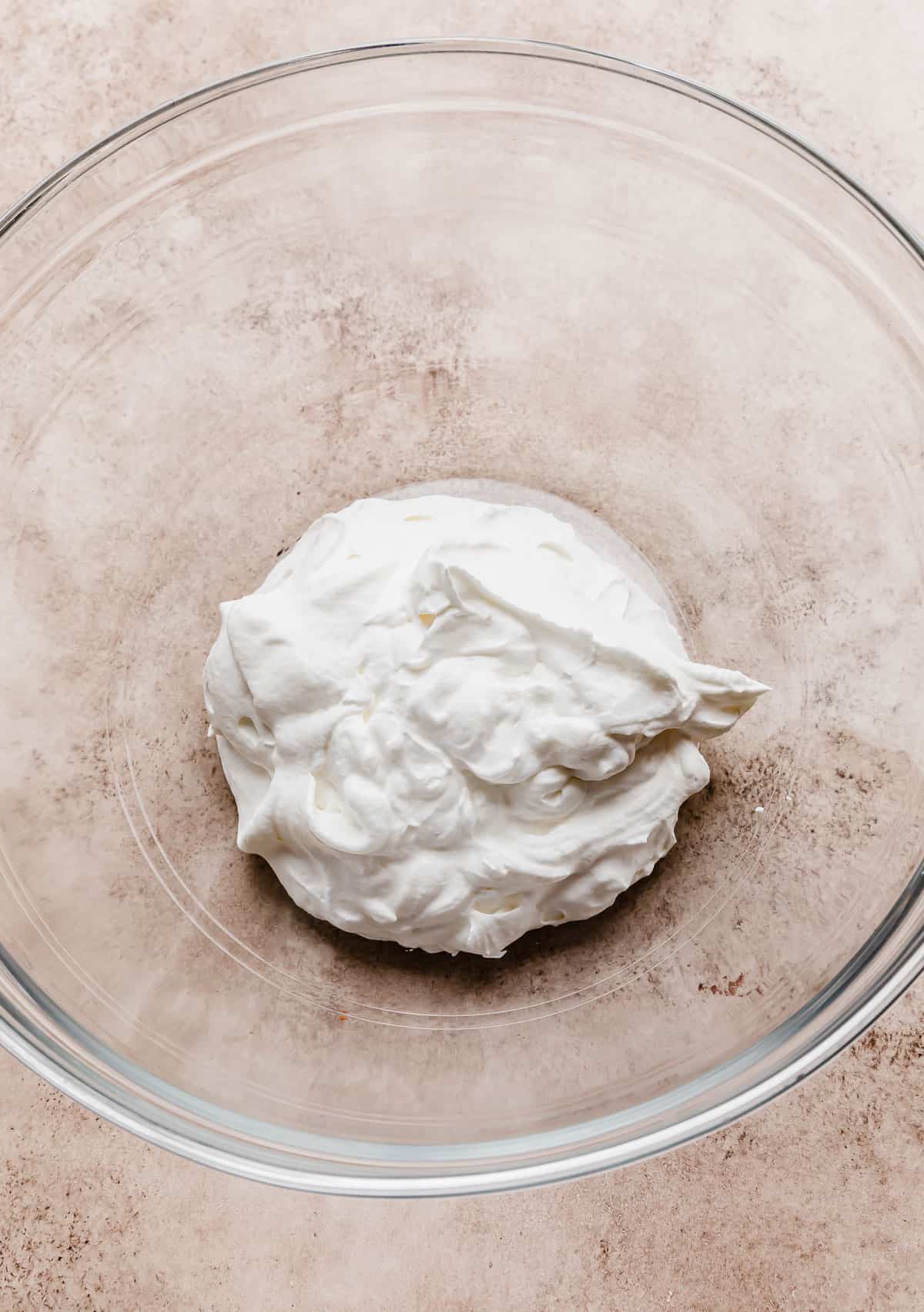 A small amount of whipped cream in a glass bowl on a light beige background.
