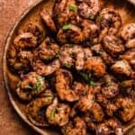 Close up photo or cooked Blackened Shrimp covered in spices and topped with fresh parsley, on a wood plate.