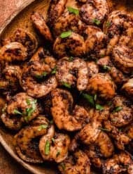Close up photo or cooked Blackened Shrimp covered in spices and topped with fresh parsley, on a wood plate.
