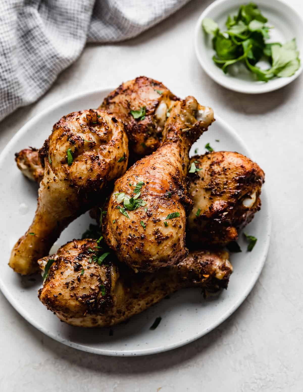 Golden and crispy Air Fryer Chicken Legs on a white plate garnished with fresh parsley.