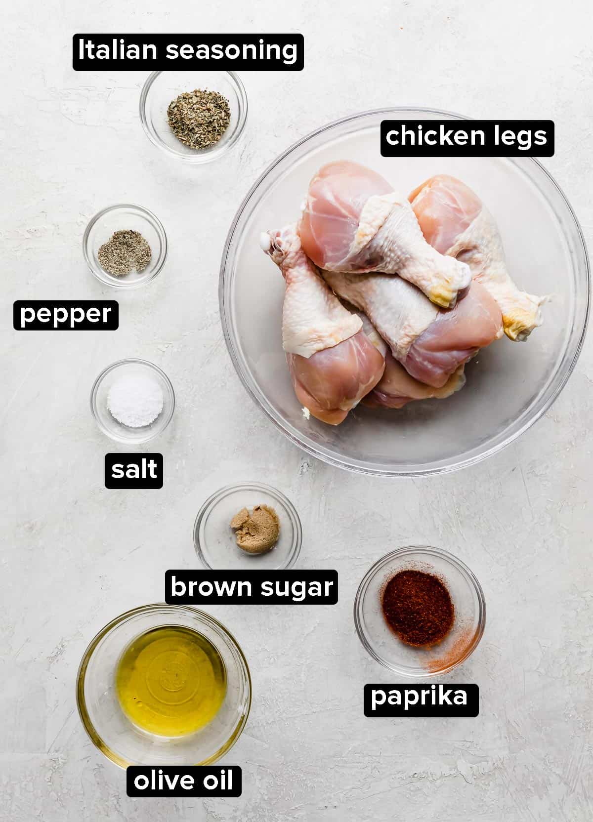 Air Fryer Chicken Legs ingredients portioned into glass bowls: chicken drumsticks, paprika, olive oil, salt, Italian seasoning, and brown sugar.