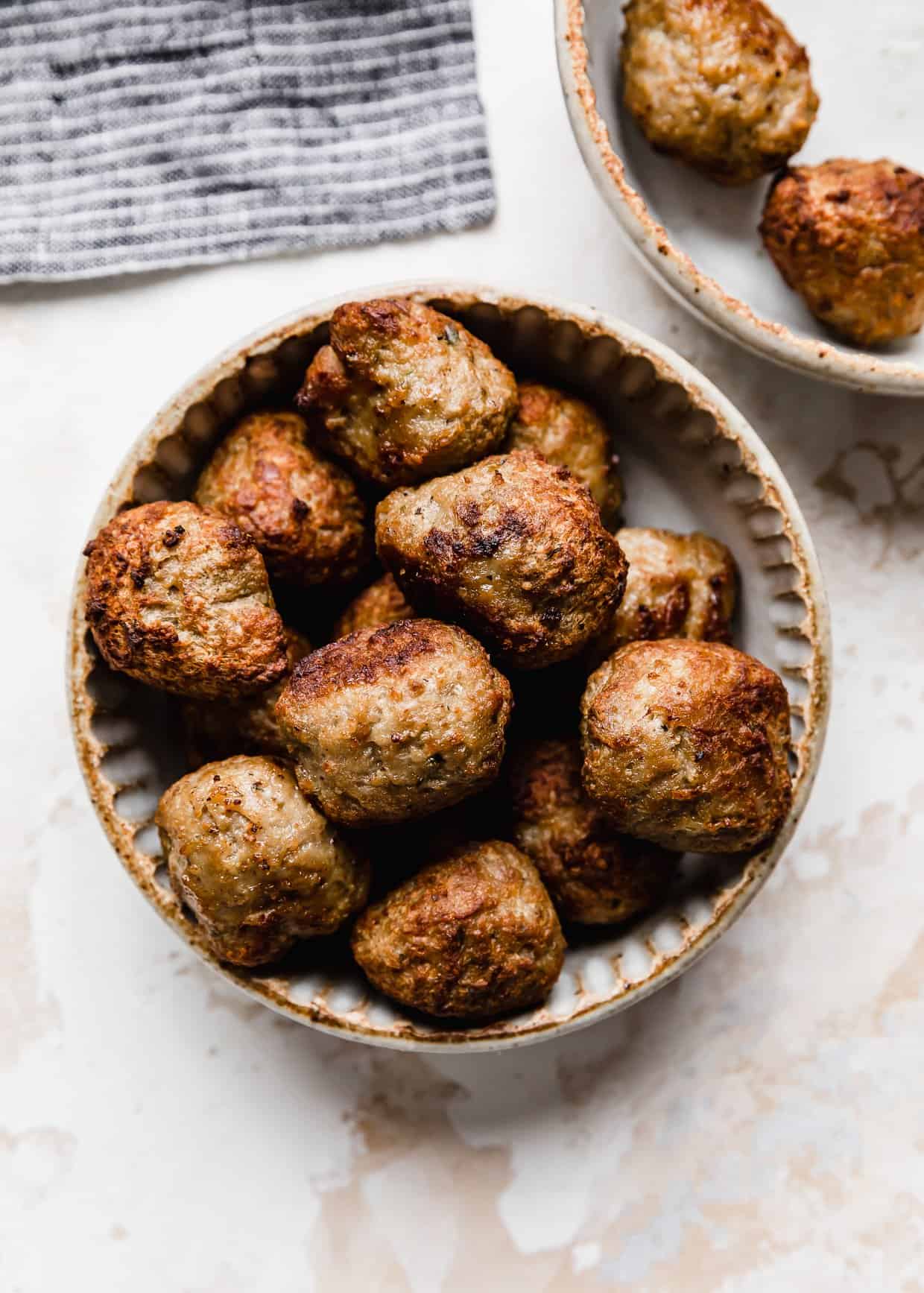Golden brown and crisped Air Fryer Frozen Meatballs in a ceramic bowl on a white textured background.