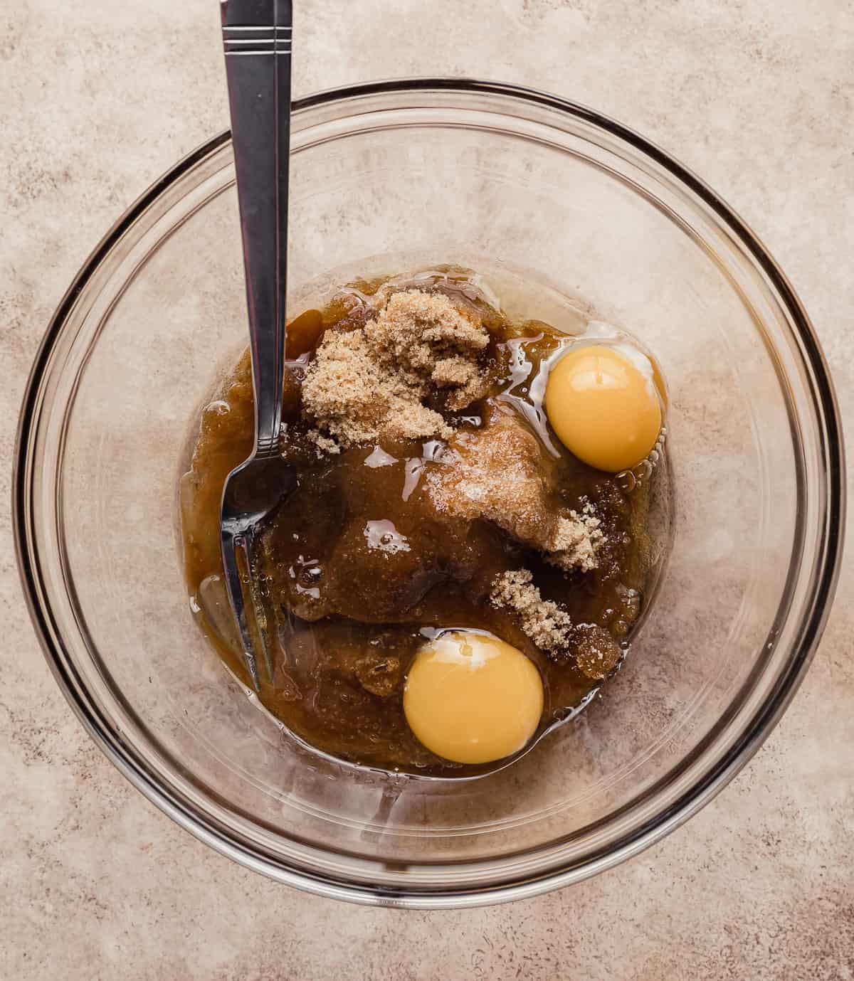 A glass bowl filled with brown sugar, two eggs, and oil for making an easy bran muffin recipe.
