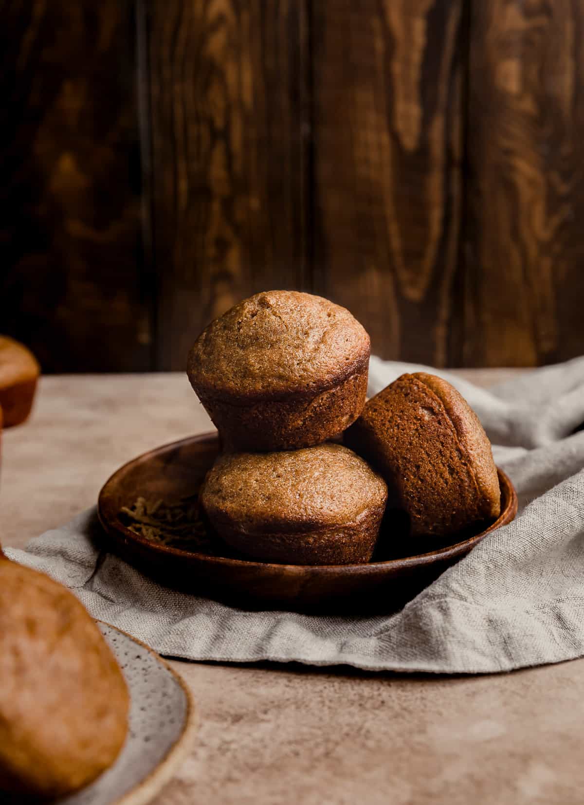 All Bran Muffins with buttermilk stacked on a small wooden plate against a wooden background.