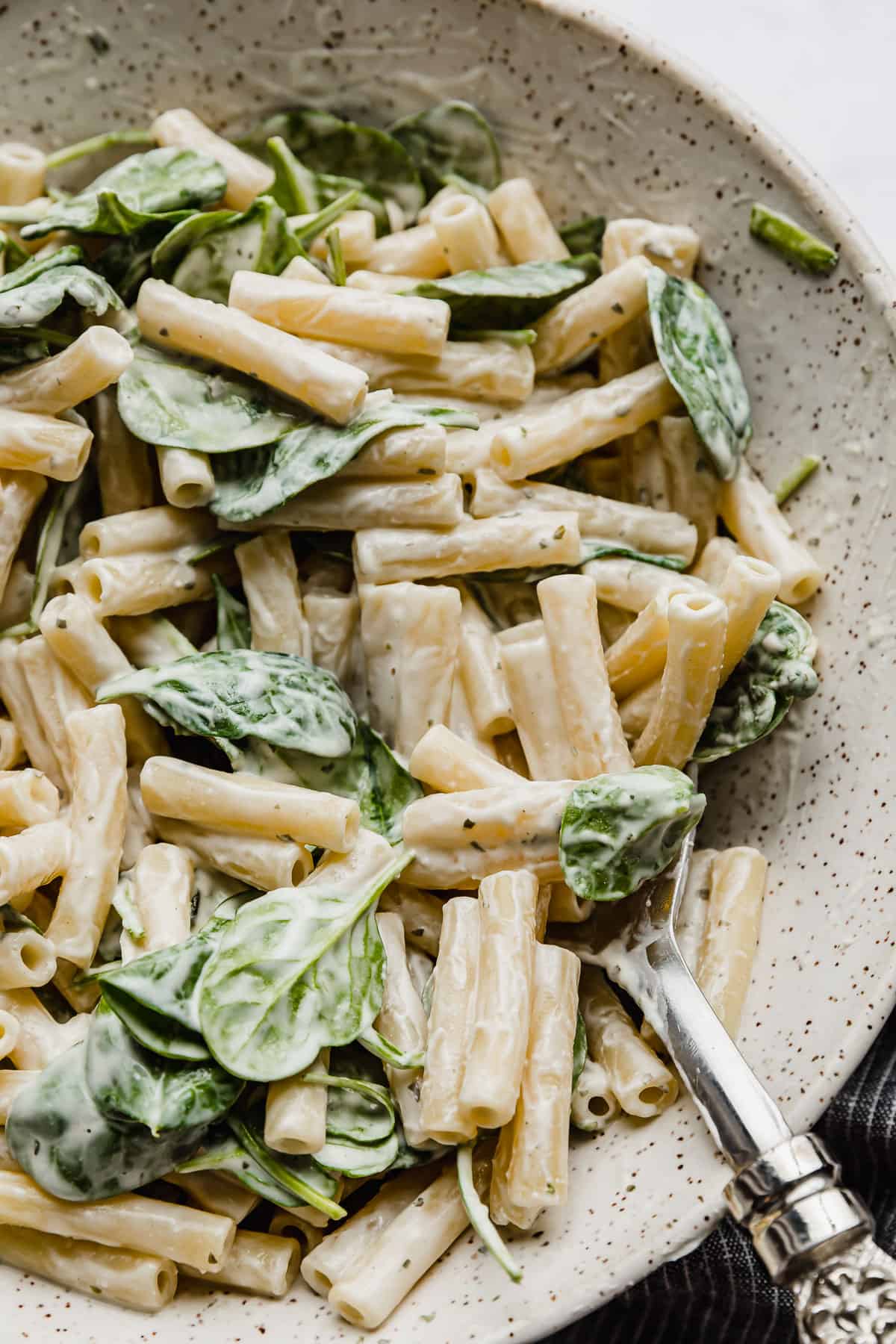 Creamy Boursin pasta recipe tossed with spinach in a serving bowl with a serving spoon in the bowl. 