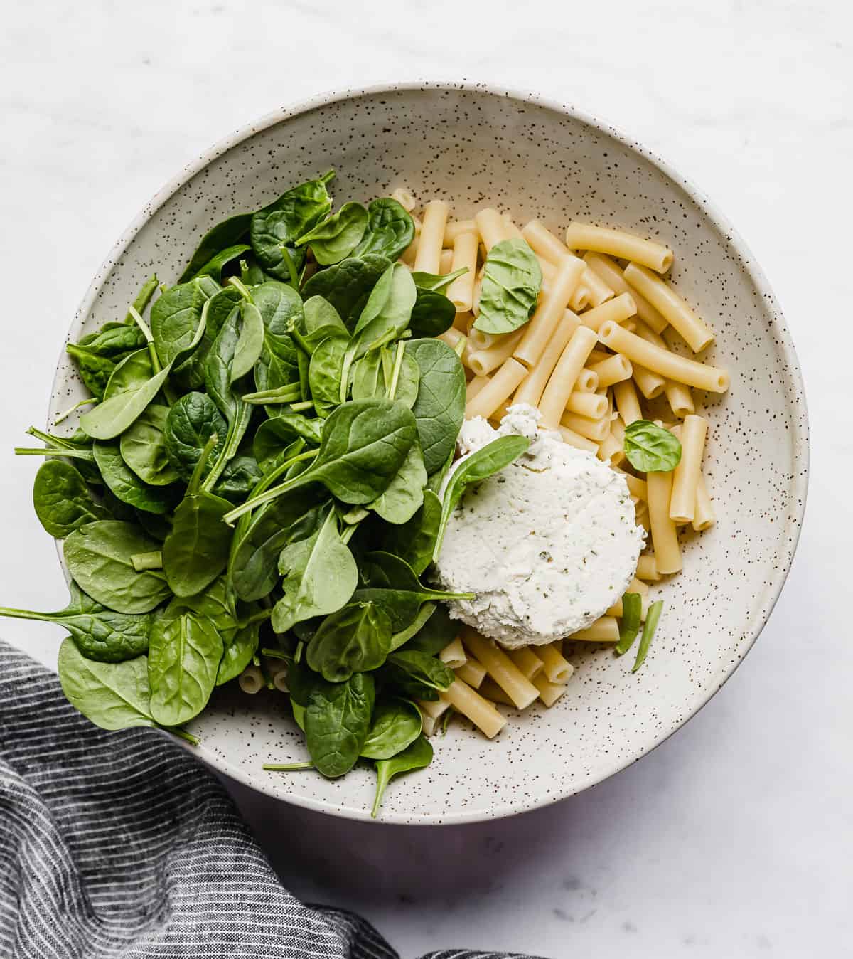 A bowl with cooked pasta noodles, chopped spinach and boursin cheese in it.