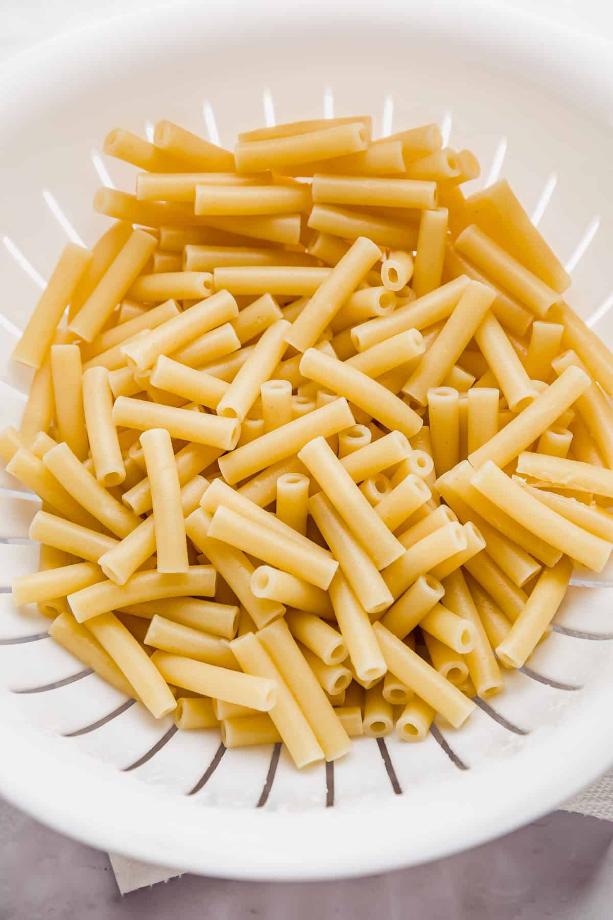 Cooked ziti pasta noodles in a white colander.