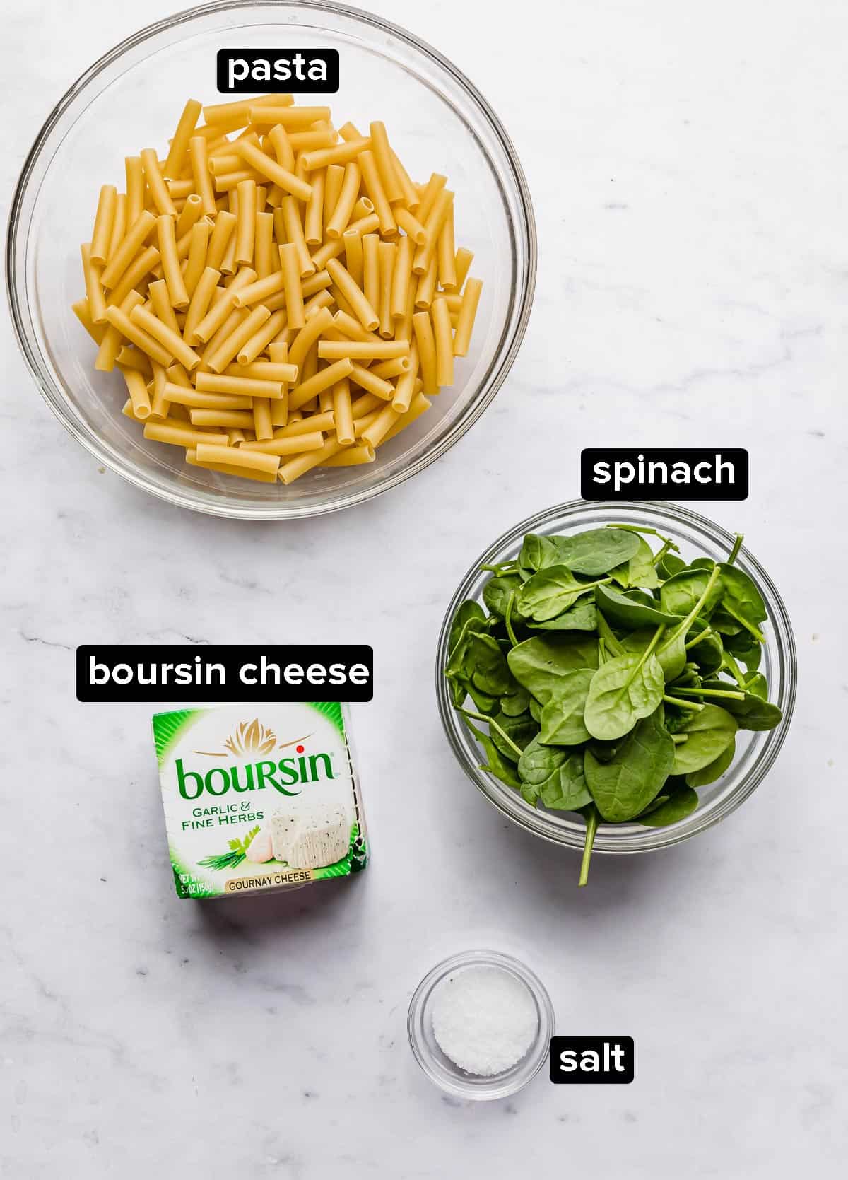 Boursin Pasta recipe ingredients on a white marble background: spinach, pasta, boursin cheese, salt.