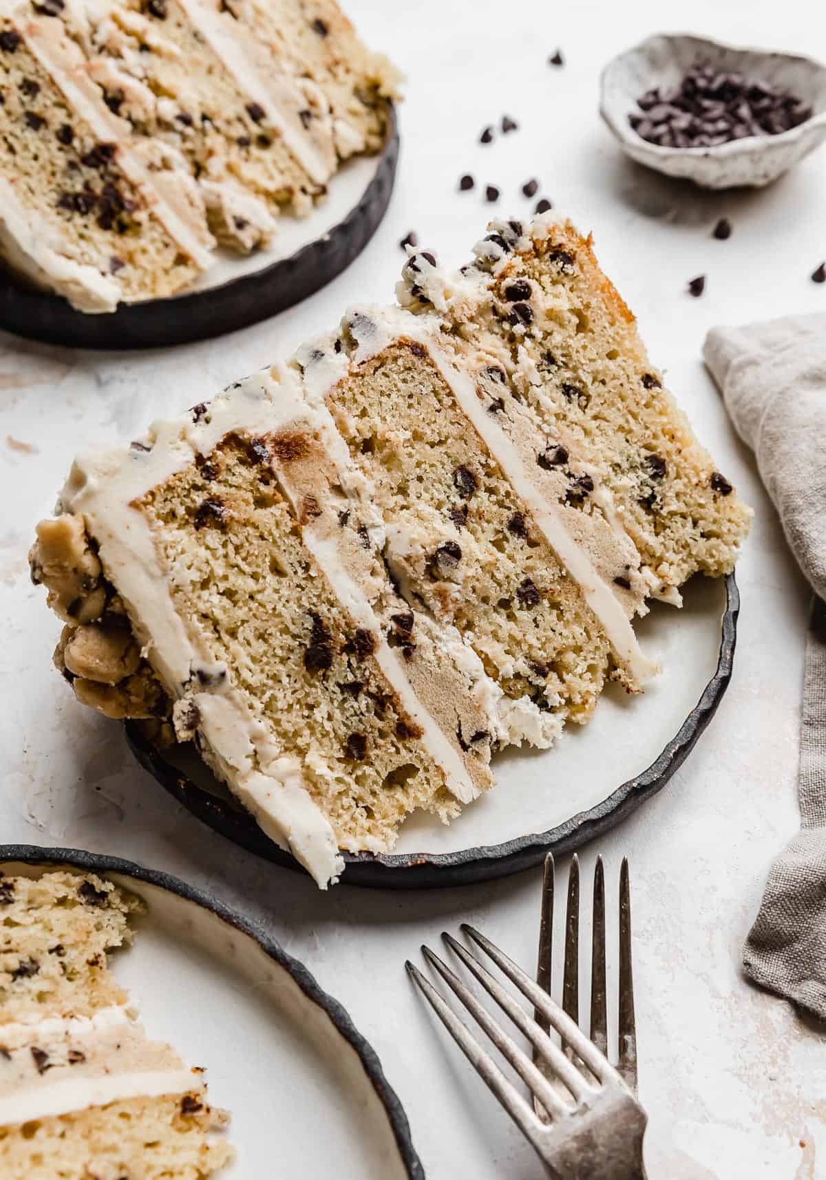 A slice of Cookie Dough Cake that has edible cookie dough between each cake layer, on a black rimmed white plate.