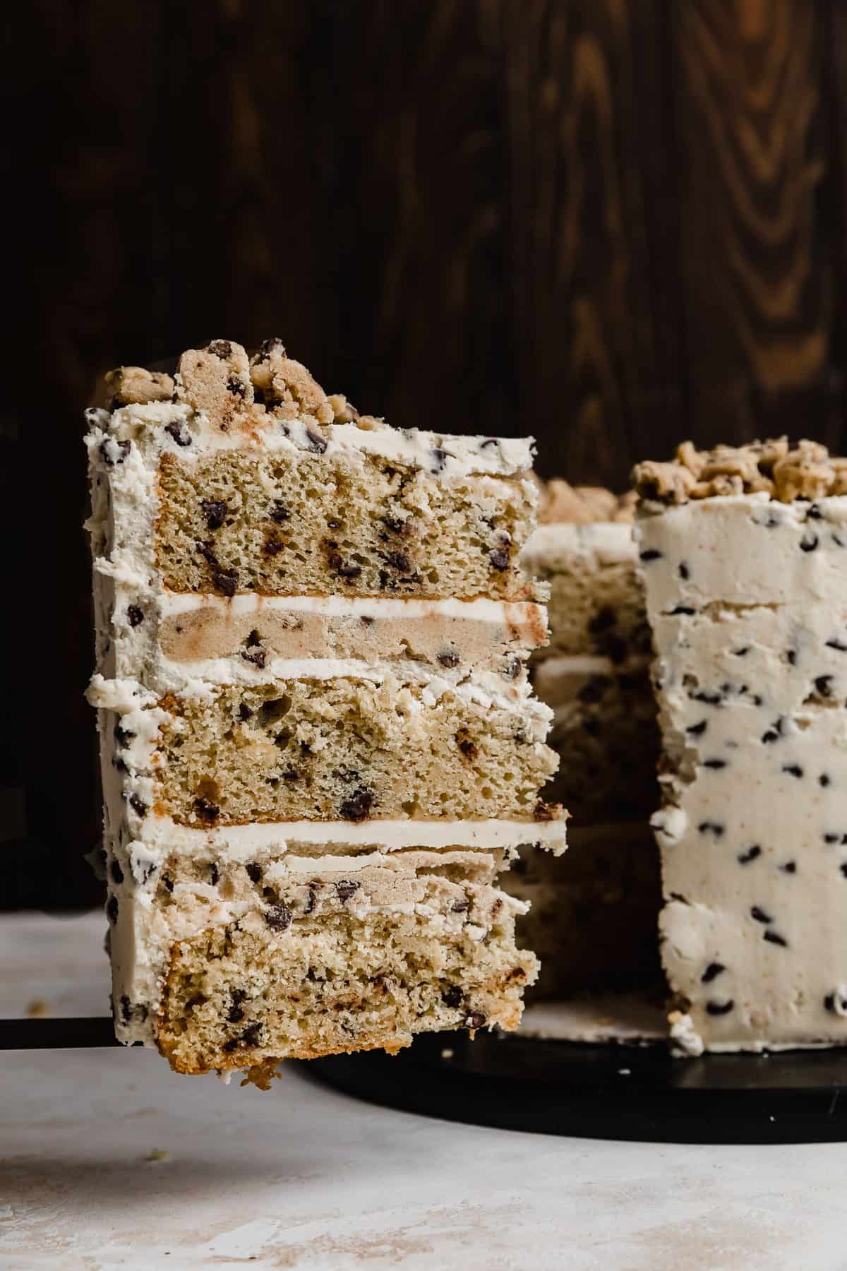 A slice of cookie dough layered cake on a serving spatula against a black background.
