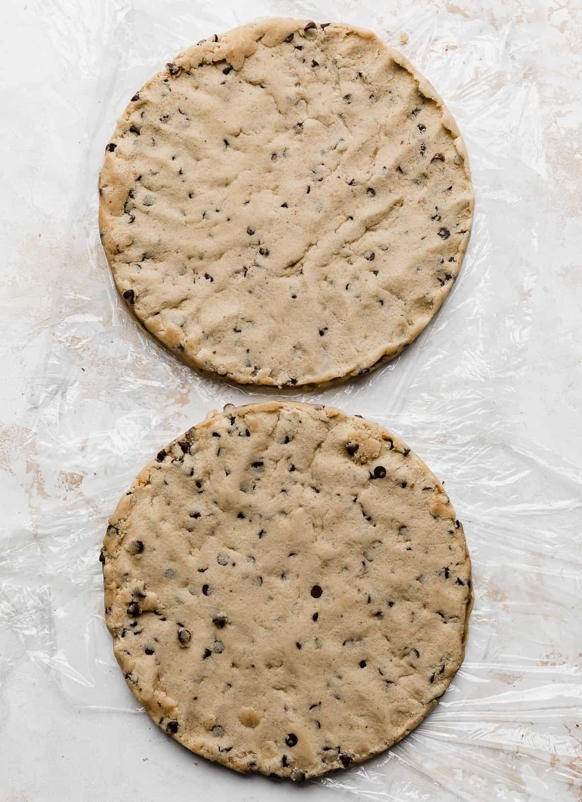 Two round disks of edible cookie dough on a white background.