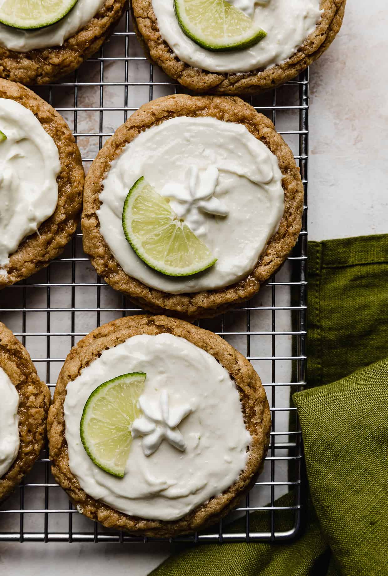 Copycat Crumbl Key Lime Pie Cookies on a wire cooling rack with a green linen napkin in the bottom right corner.
