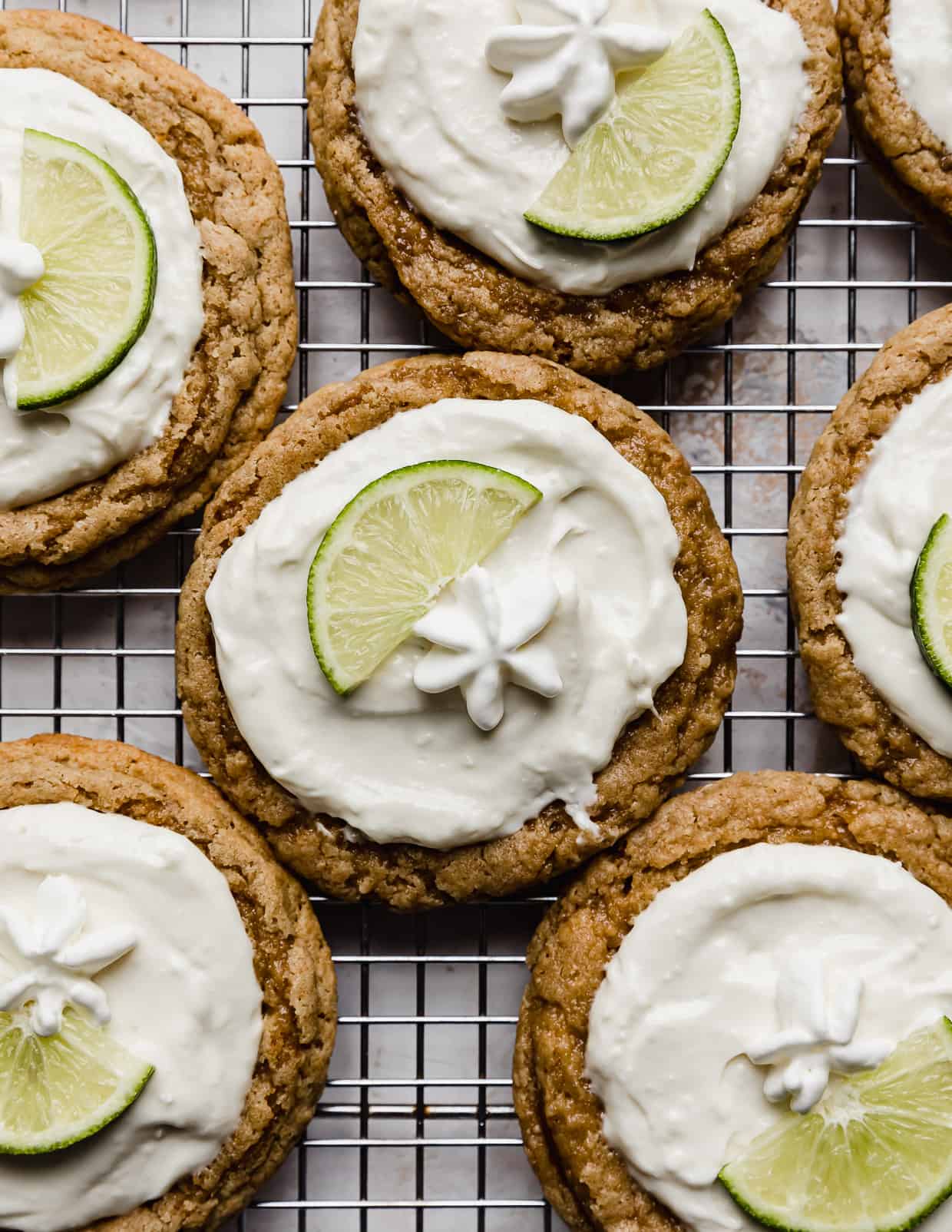 Crumbl Key Lime Pie Cookies topped with whipped topping and a lime wedge on a wire cooling rack.