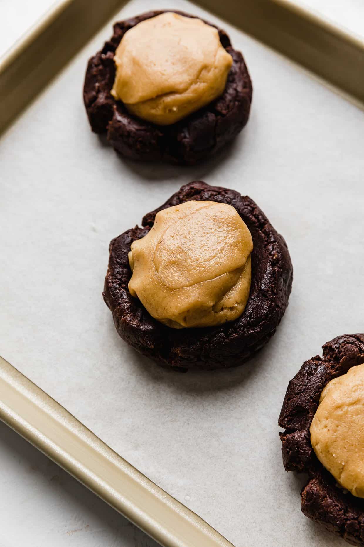 A ball of peanut butter cookie dough on top of a brownie cookie dough ball.