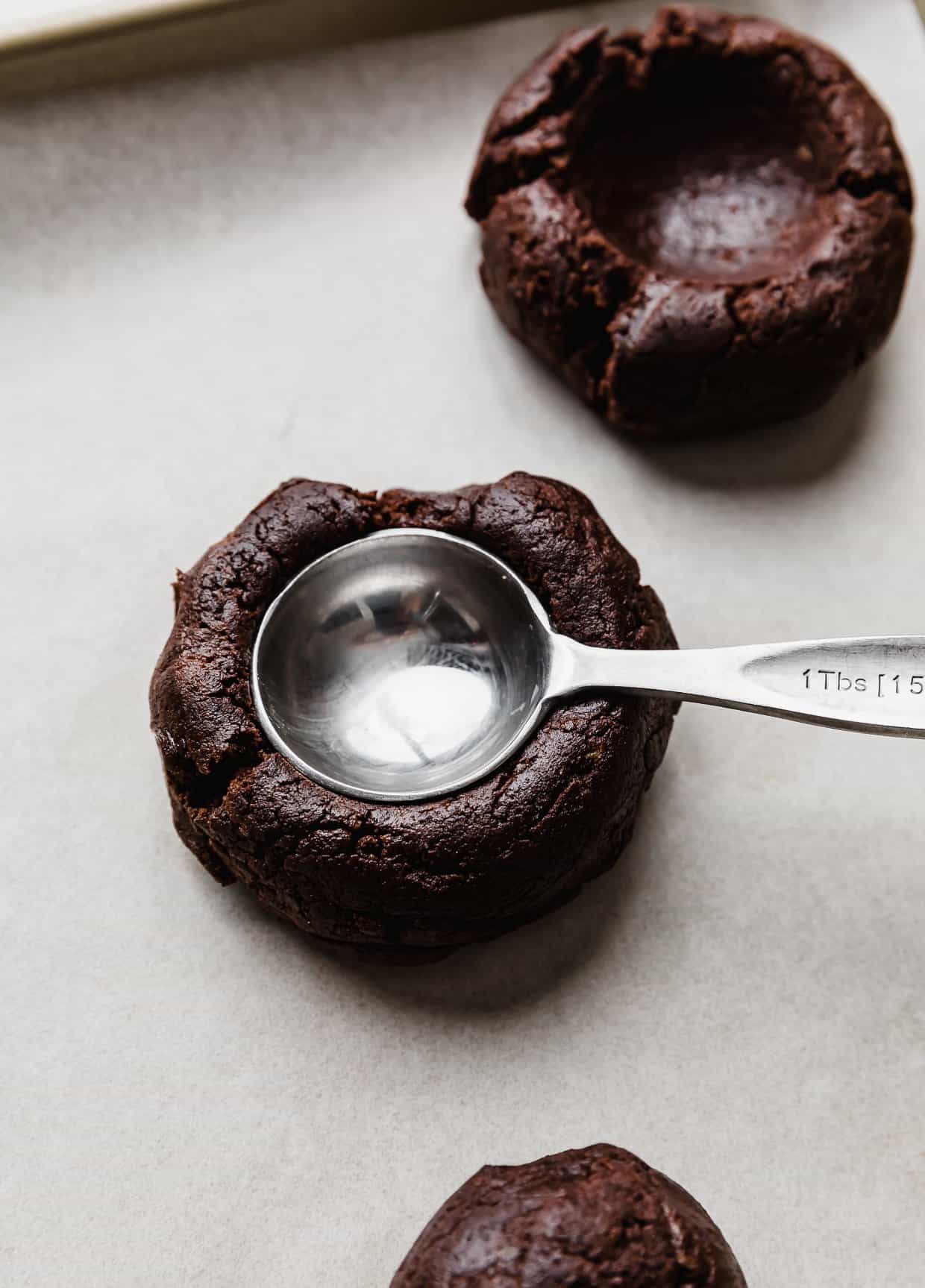 A brown cookie dough ball with a tablespoon pressing into the dough.