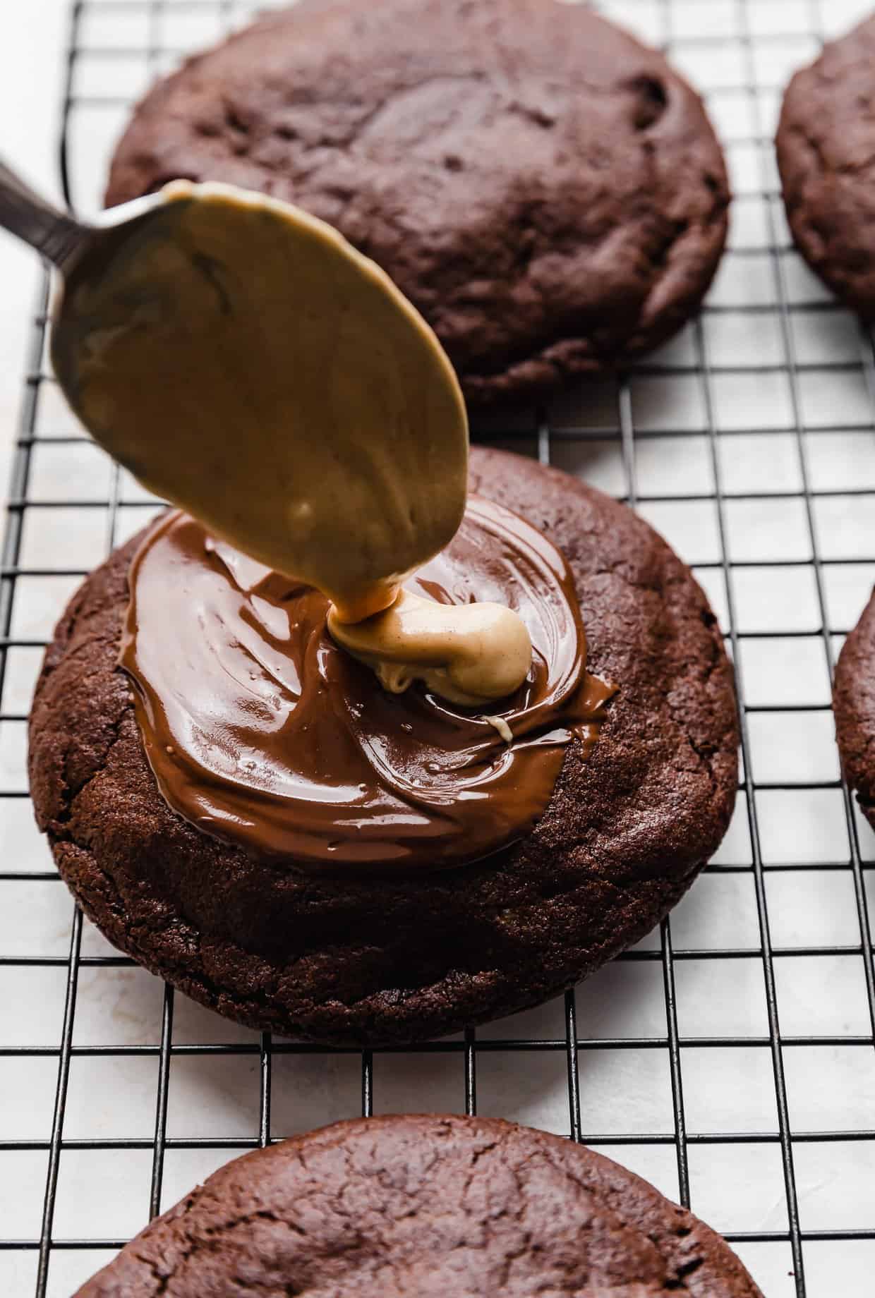 A spoon dolloping melted peanut butter overtop a copycat Crumbl Peanut Butter Brownie Cookie.