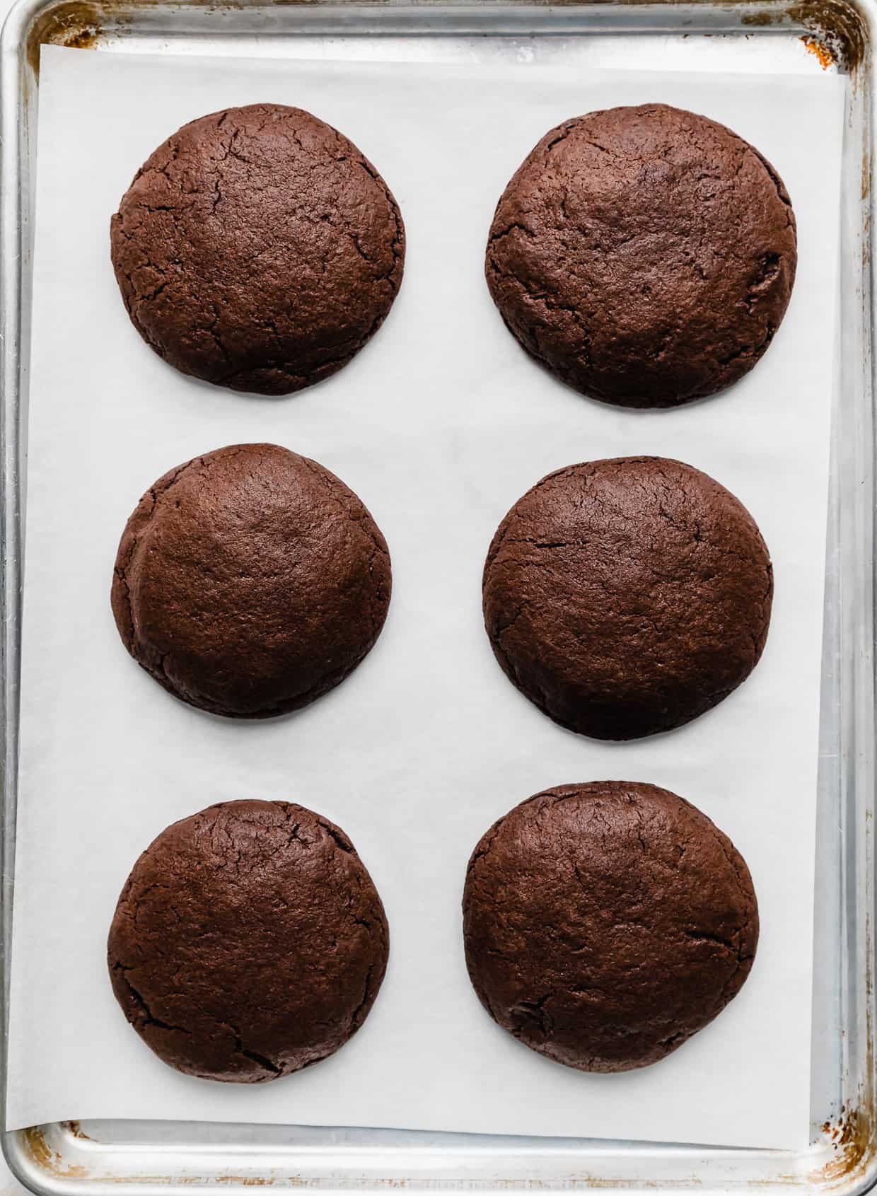 Six baked brownie cookies on a white parchment paper.