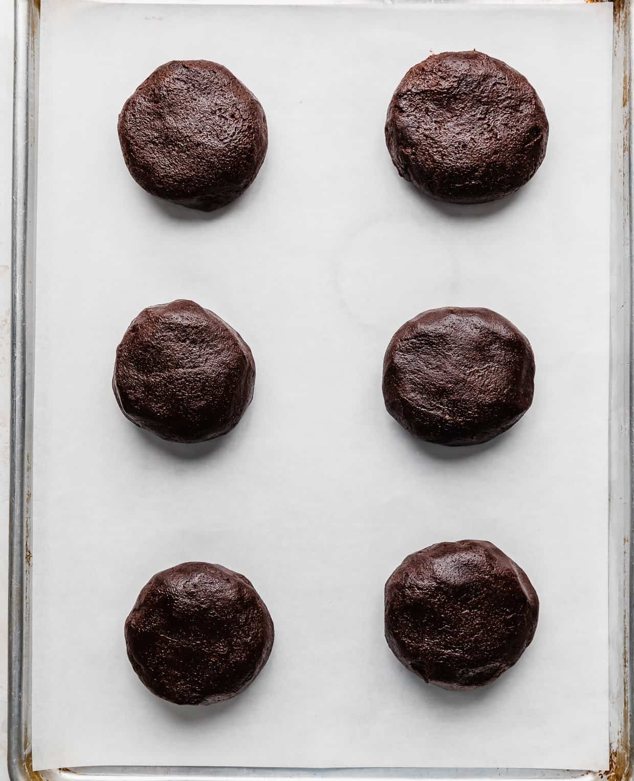 Six Peanut Butter Brownie Cookie dough balls on a white parchment lined baking sheet.