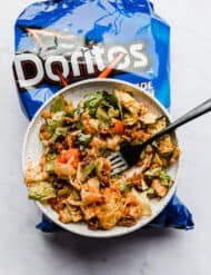 Doritos Taco Salad on a white plate sitting on a blue bag of Doritos Cool Ranch chips.