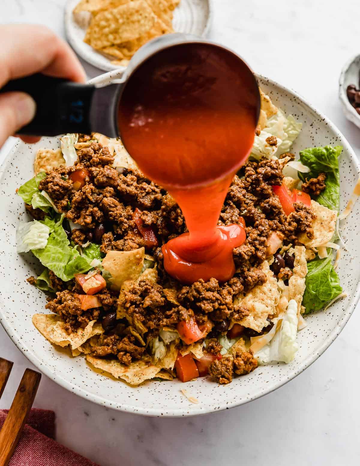 Catalina dressing being poured overtop a cool ranch Doritos Taco Salad in a white bowl.