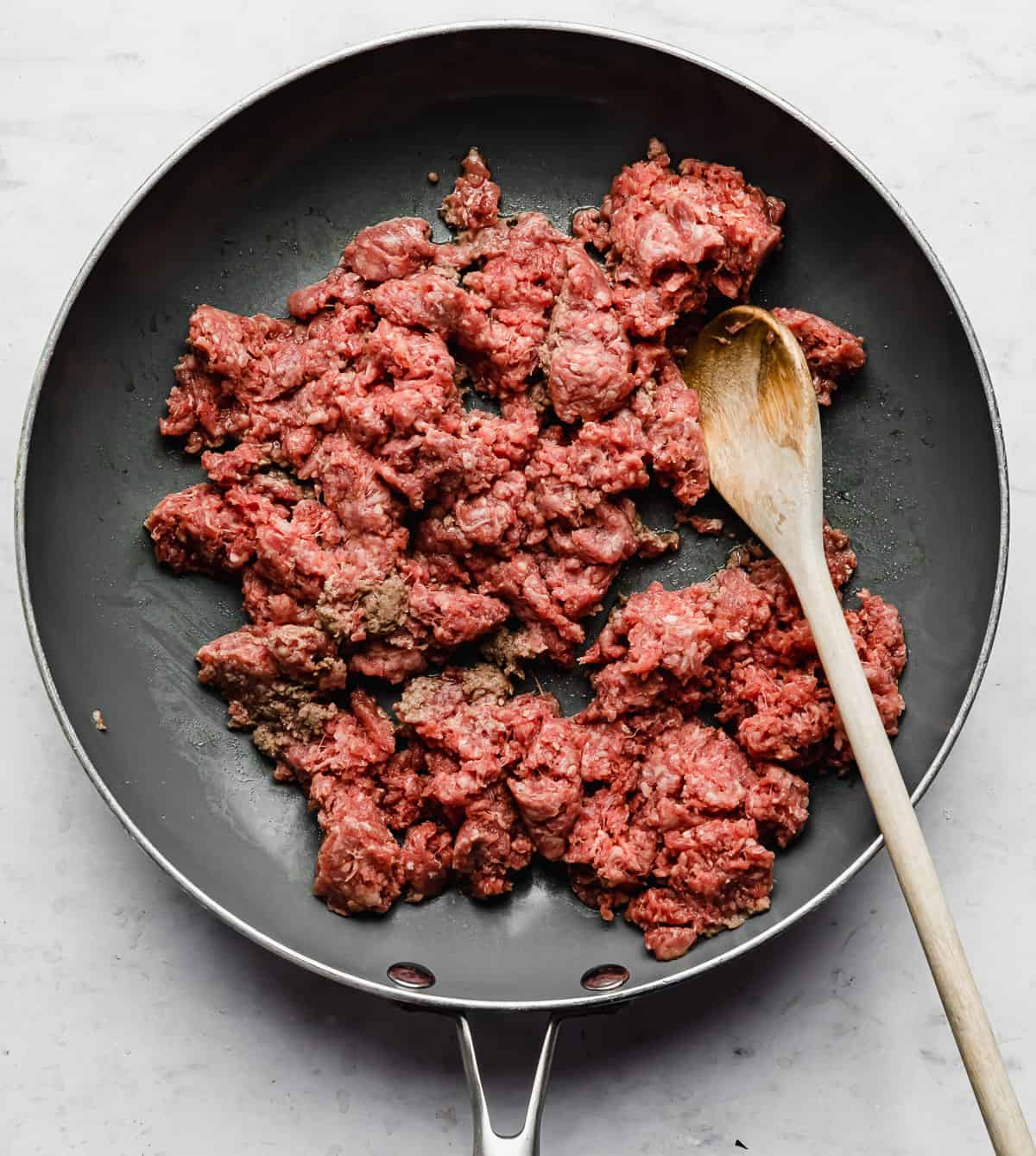 Raw ground beef in a grey skillet on a white background.