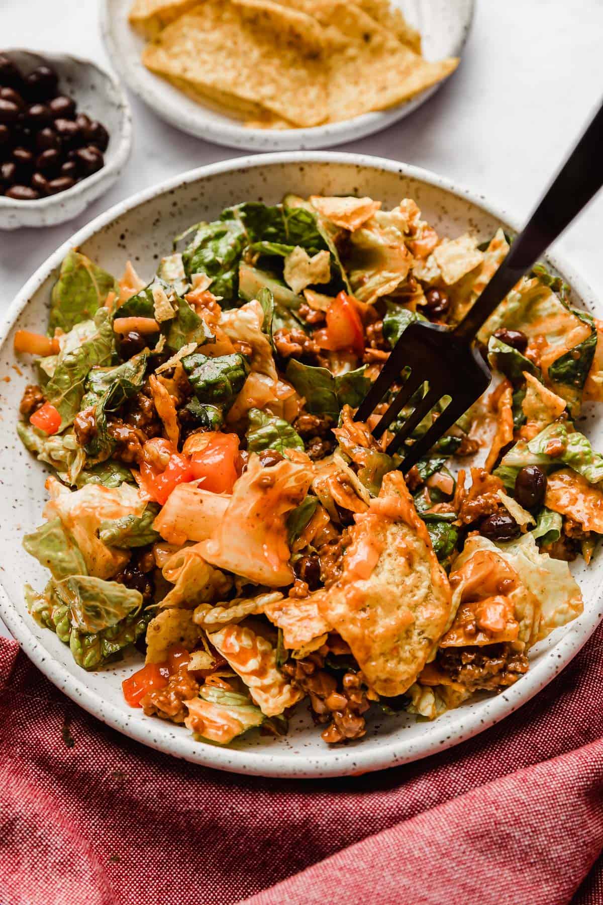 Doritos Taco Salad with Catalina dressing overtop, on a white plate with a black fork piercing lettuce.