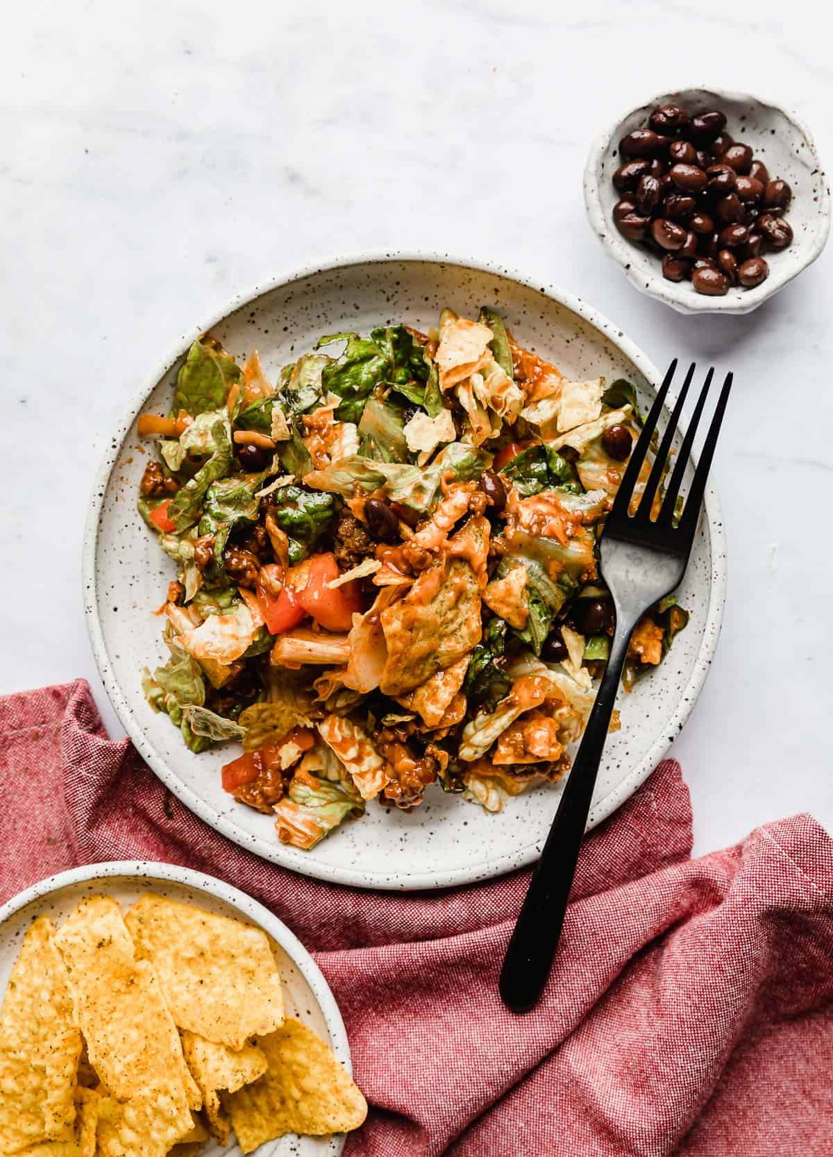 A taco salad with Catalina dressing overtop, on a white background with a red napkin under the plate.