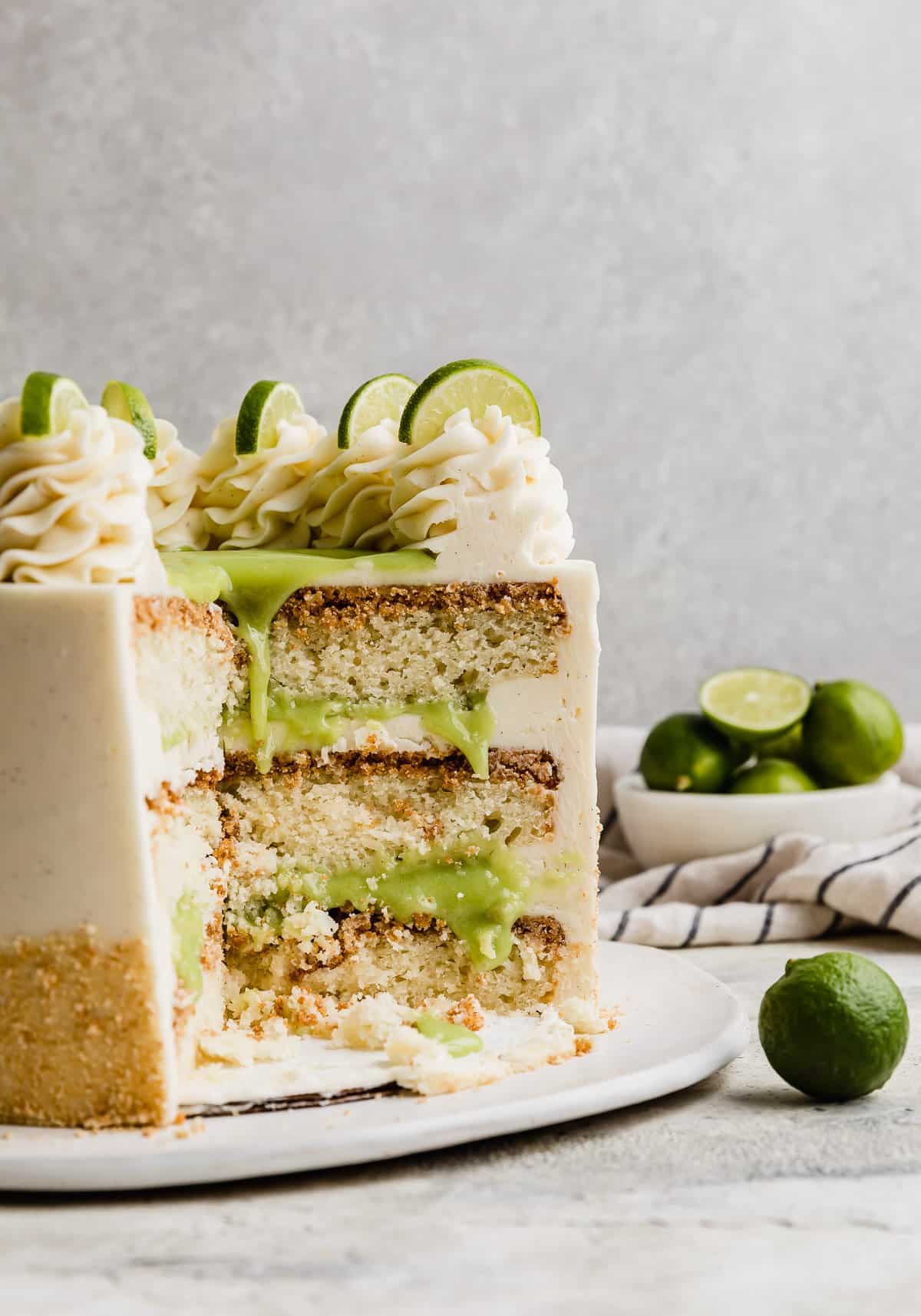 A Key Lime Cake Recipe cut, exposing the three slices of lime cake baked on graham cracker crusts and filled with a light green key lime curd and white frosting.