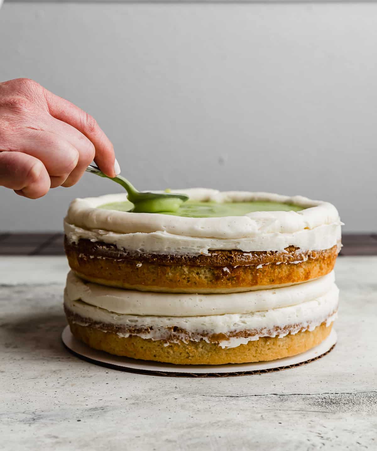 A spoon spreading a light green key lime curd filling on top of a two tiered key lime pie cake.